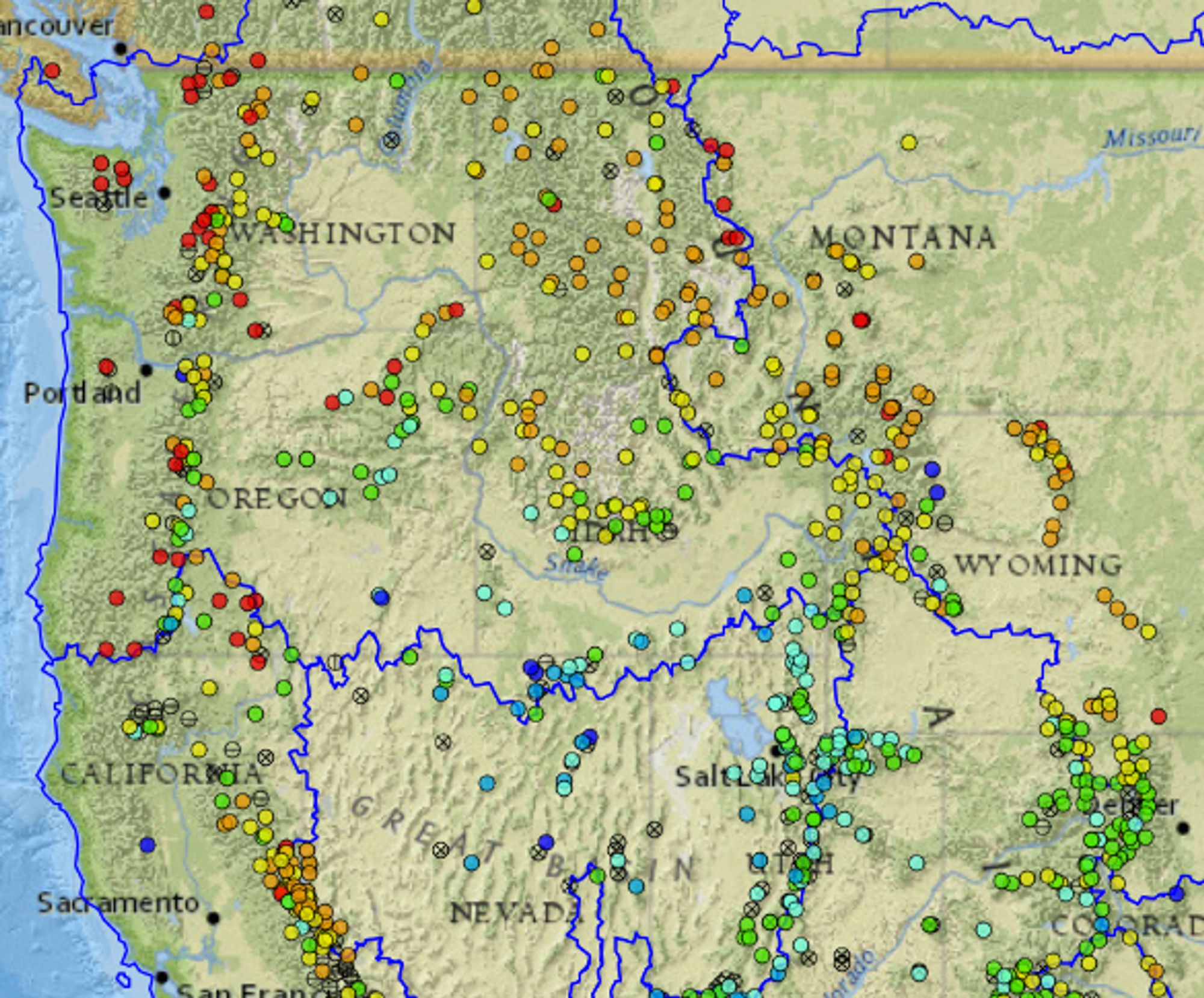 Map with dots representing snow accumulation measurement sites across the western US. Northern sites are red or orange indicating low snowpack relative to median, southern sites green or blue (close to or above the median)