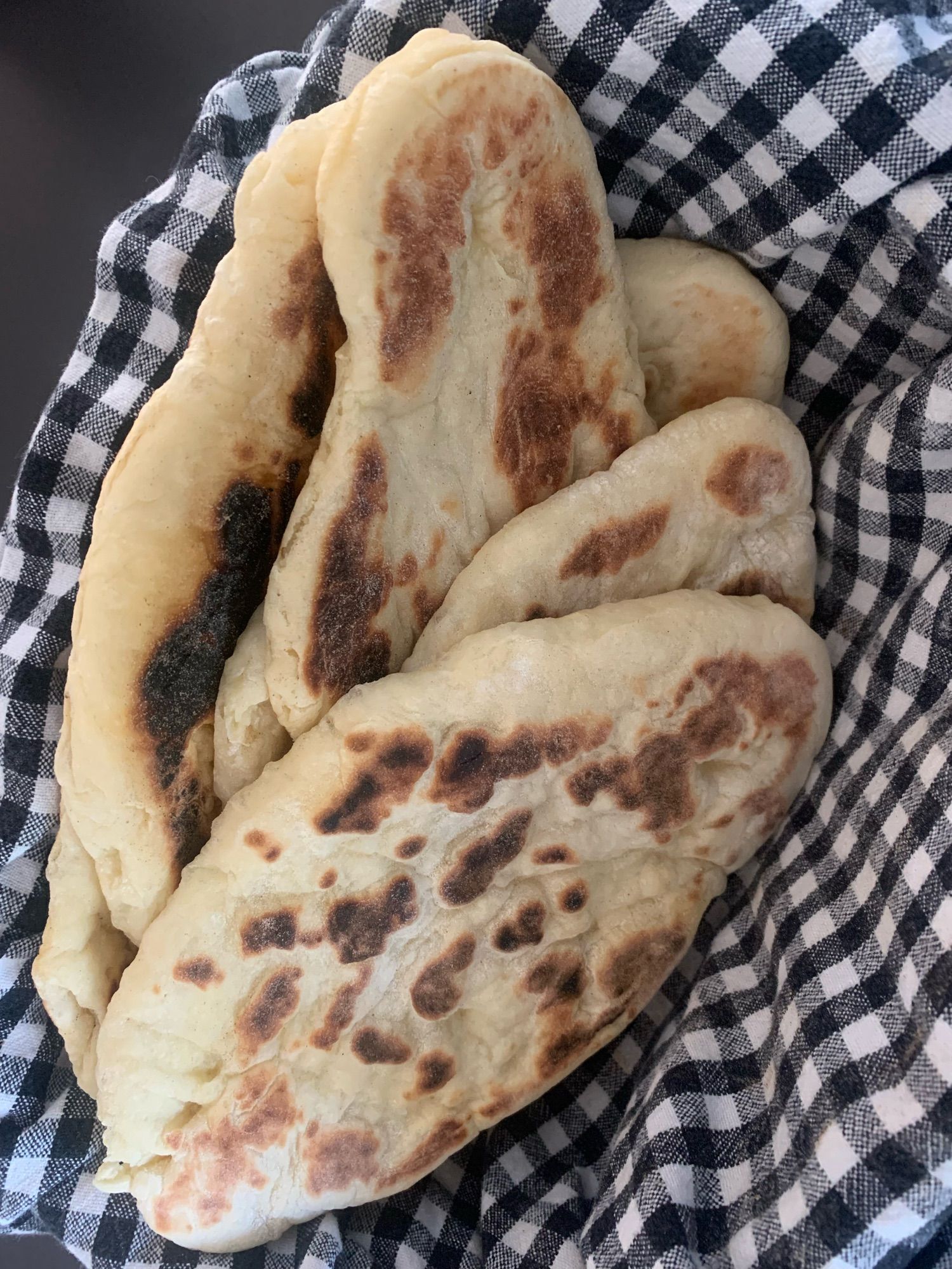 A basket lined with a tea towel containing freshly made naan bread straight out of the skillet.  Not pictured: garlic-infused ghee, to be applied with a brush before serving