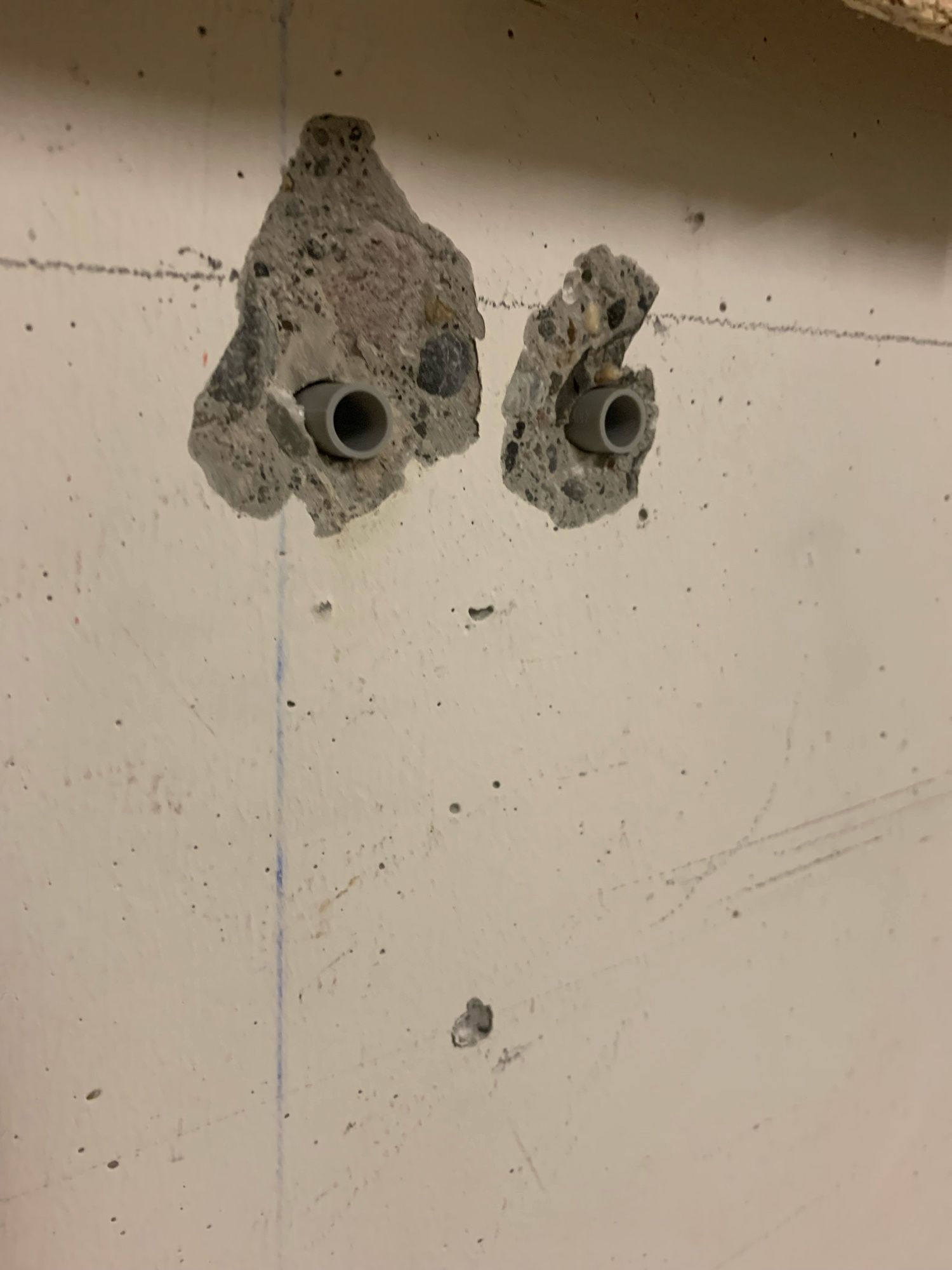 three holes drilled in the cement wall form a face, with eyes at the top and a small open mouth at the bottom.  this one is very surprised at something