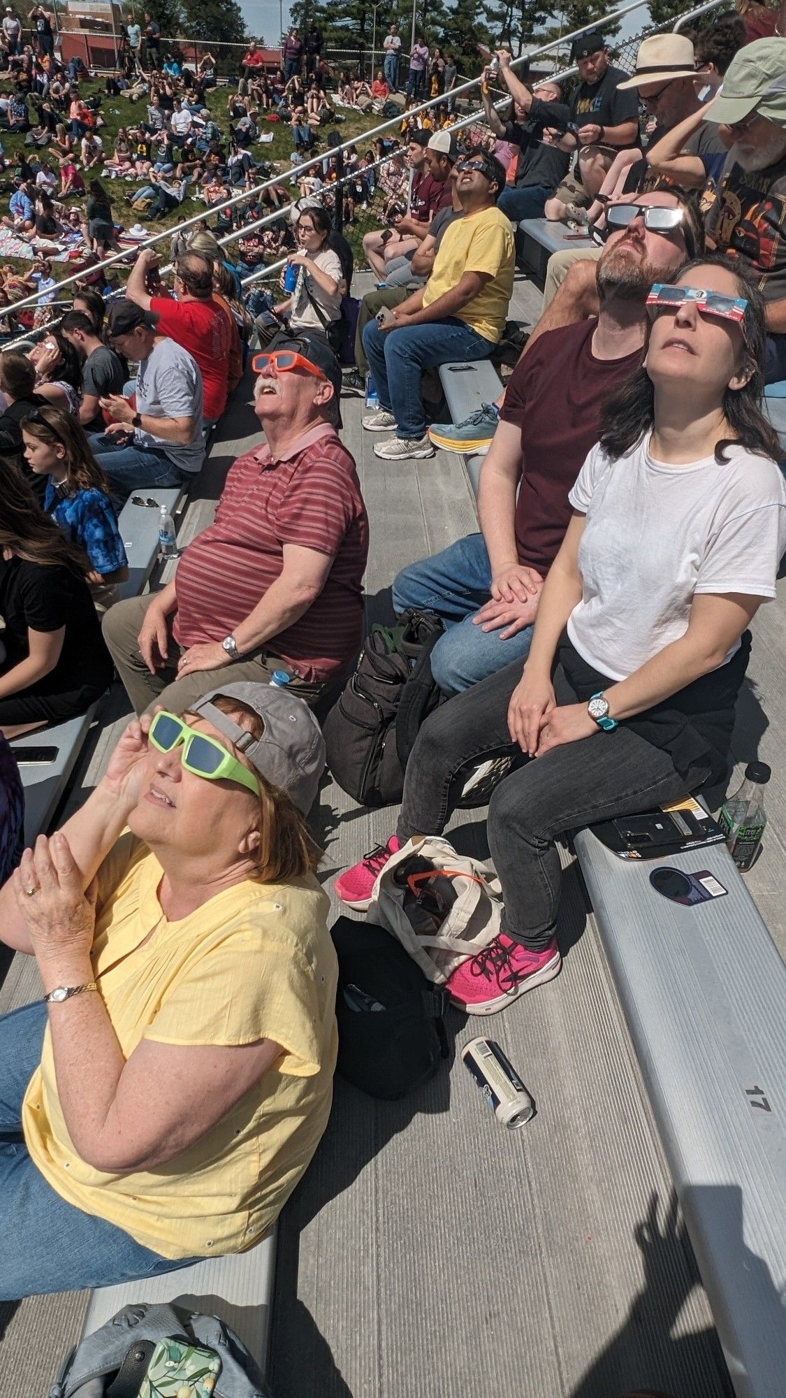 Family members in the bleachers look at the sun, wearing eclipse glasses