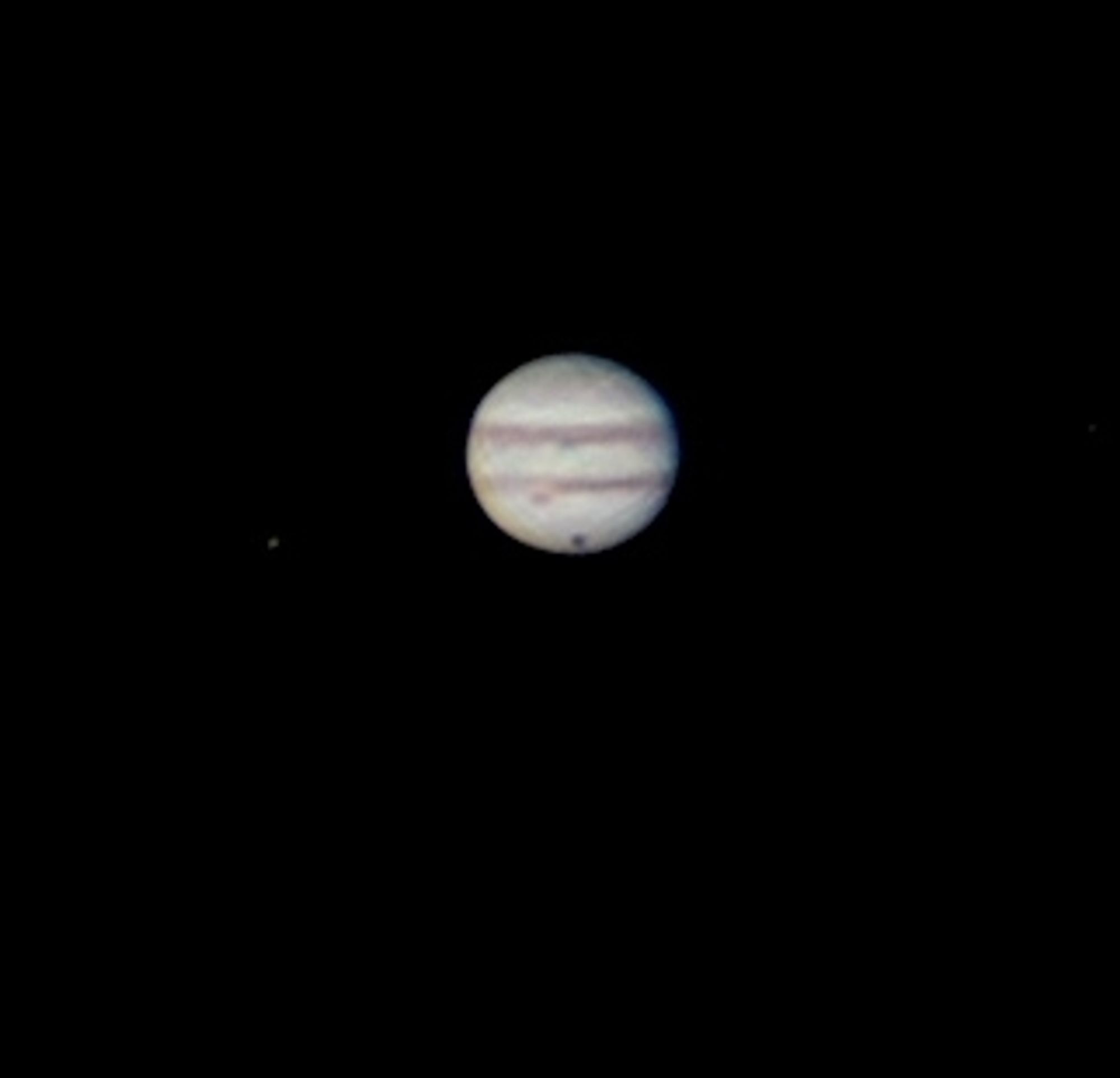 The gas giant planet, Jupiter. It has alternating colors of light and dark cloud bands. It has two dark reddish cloud bands above and below it's middle. Below the bottom band is it's famous Great Red Spot. And almost at the very bottom of the planet is the dark shadow of it's big moon, Ganymede. Ganymede is the largest moon in our entire solar system.