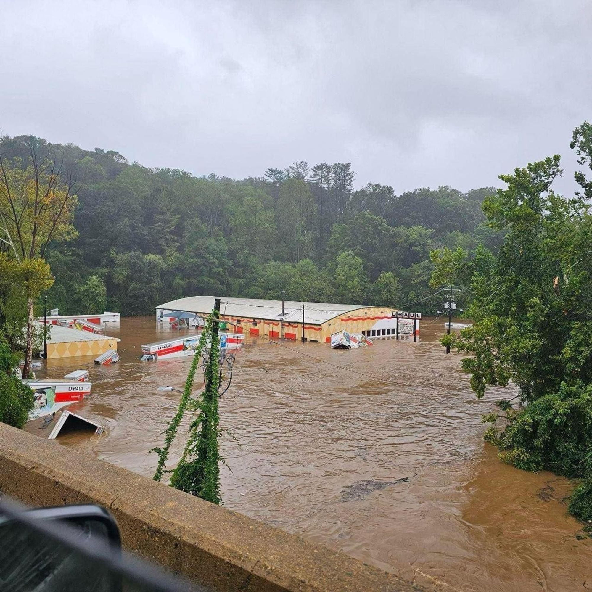 A photograph from an overpass of a flooded Uhaul center. The want is up to the windows of the trucks and buildings.