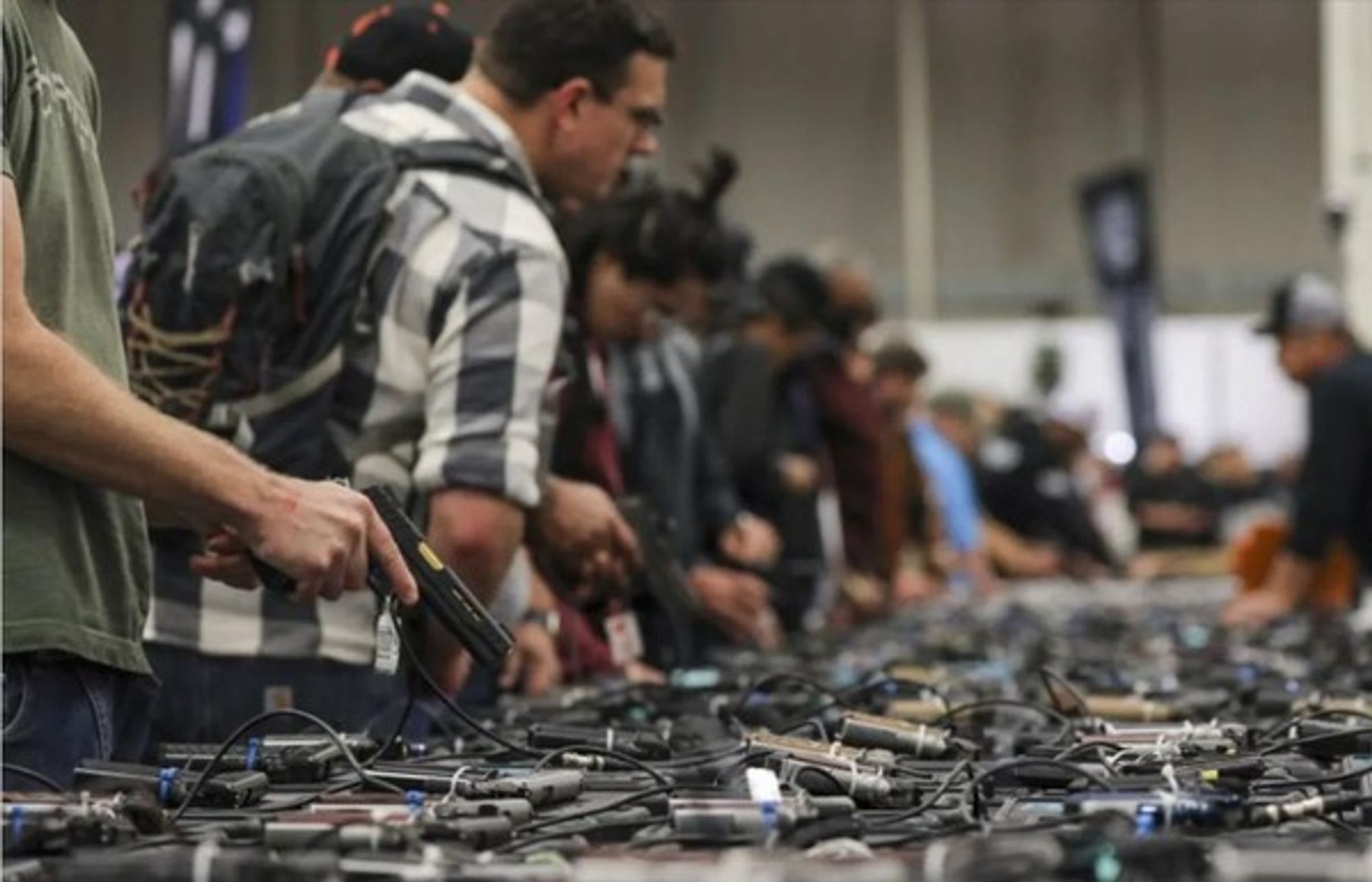 A picture of a bunch of people (it looks like all white men) looking at handguns for purchase.