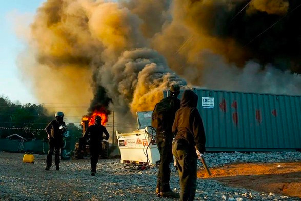 Masked demonstrators stand before smoking flames at the Cop City construction site on March 5, 2023.