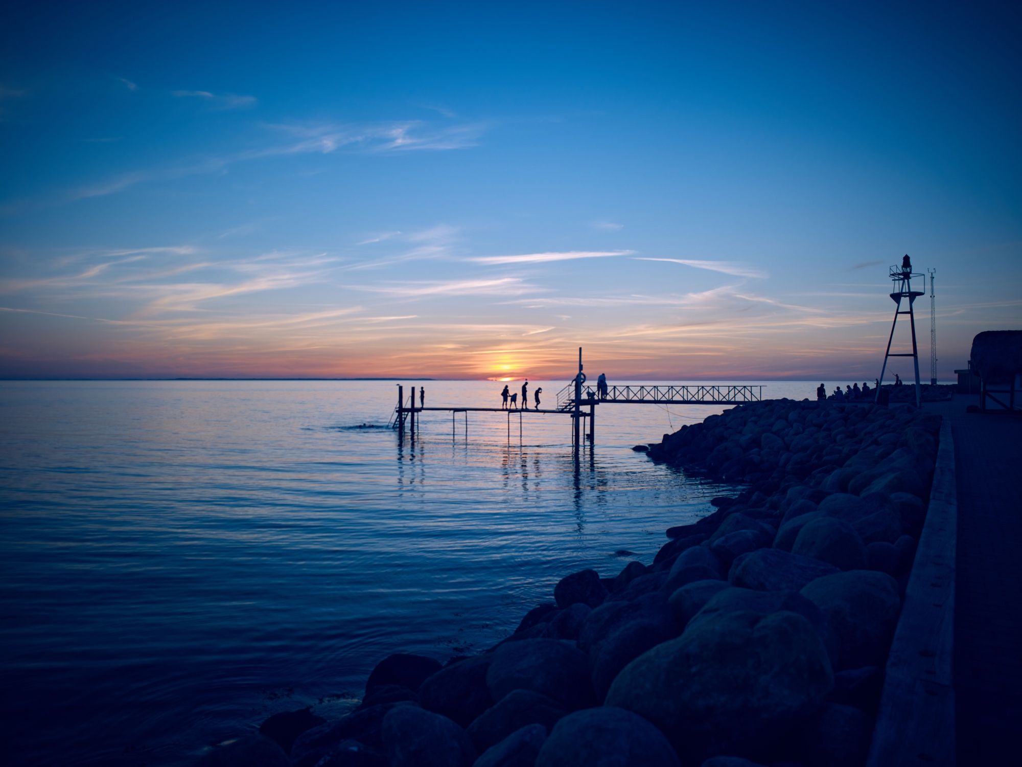 Badesteg mit mehreren Leuten an der Hafenmole in Vesterø Havn auf der dänischen Kattegat-Insel Læsø bei Sonnenuntergang.

© Torsten Grieger