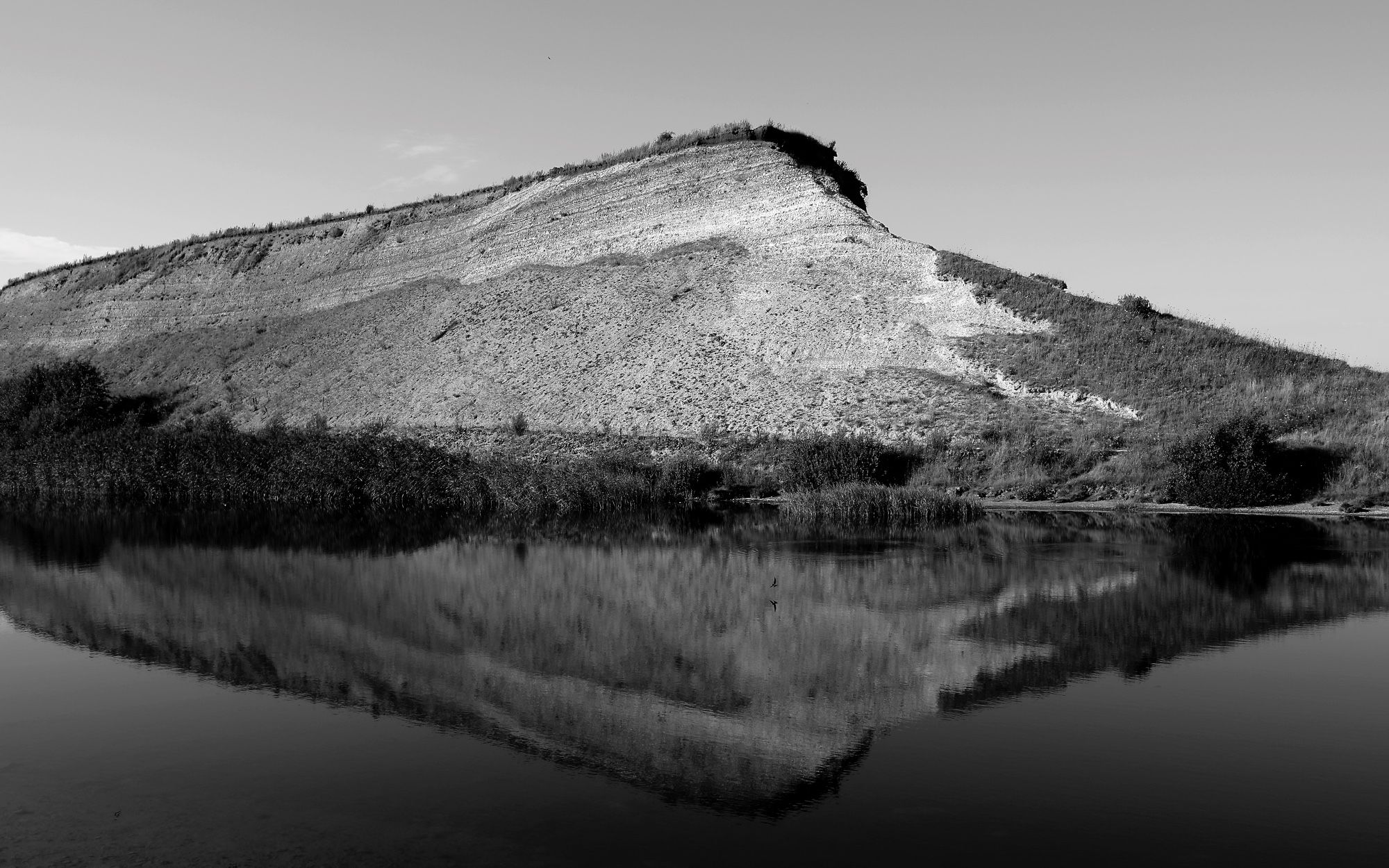 Das S/W-Foto zeigt den sich in der künstlichen Lagune am Hafen von Ejerslev spiegelnden Einschnitt einer stillgelegten Moler-Tongrube in die Küstenlandschaft auf der dänischen Limfjord-Insel Mors.

@ Torsten Grieger

Das Foto kann als #NFT auf Foundation erworben werden:
https://foundation.app/mint/eth/0x270BCE9d0AdF48209ADf1b42213Cdf0001260Ed7/7