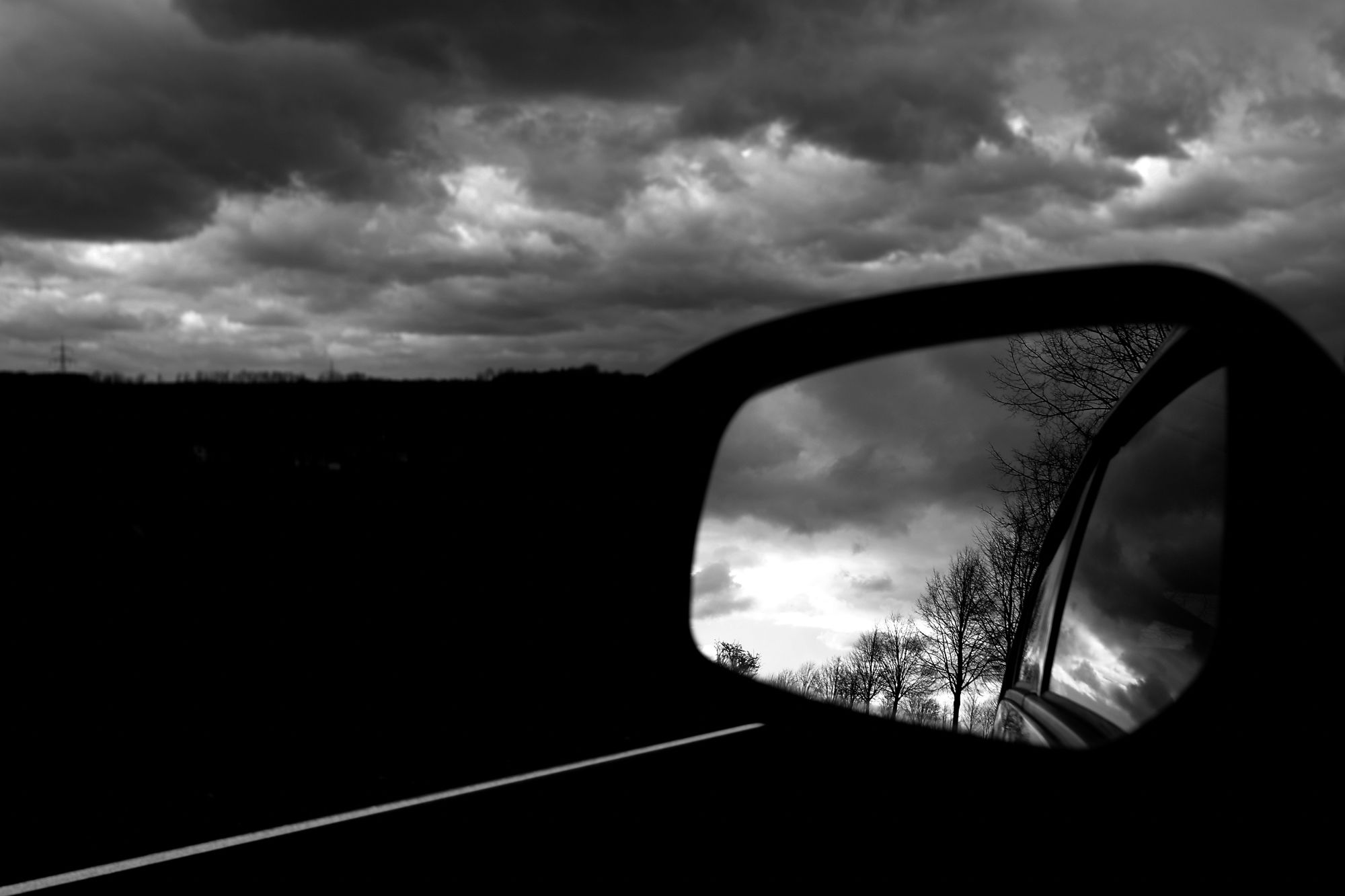 Das S/W-Foto "La Strada #01 – Look in the outside mirror" zeigt den Blick in den Außenspiegel eines Kleinwagens an einem düster-gewittrigen Tag.

@ Torsten Grieger

Das Foto kann als #NFT auf Foundation erworben werden:
https://foundation.app/mint/eth/0xB5453d9Aea9707A6012ba6a7AC651F91346c0f9A/1