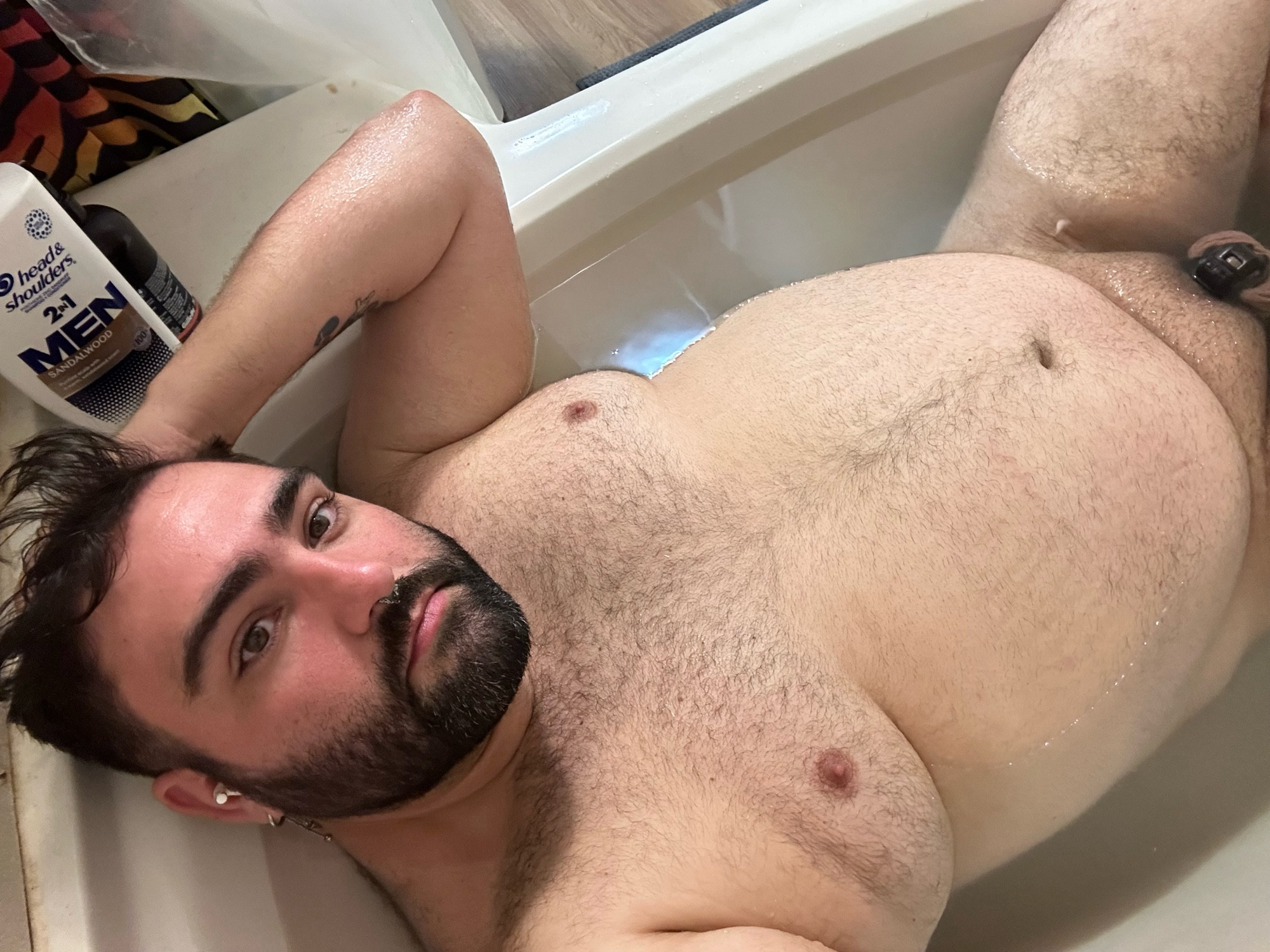 Chastity bear soaking in a warm bath with cage visible.