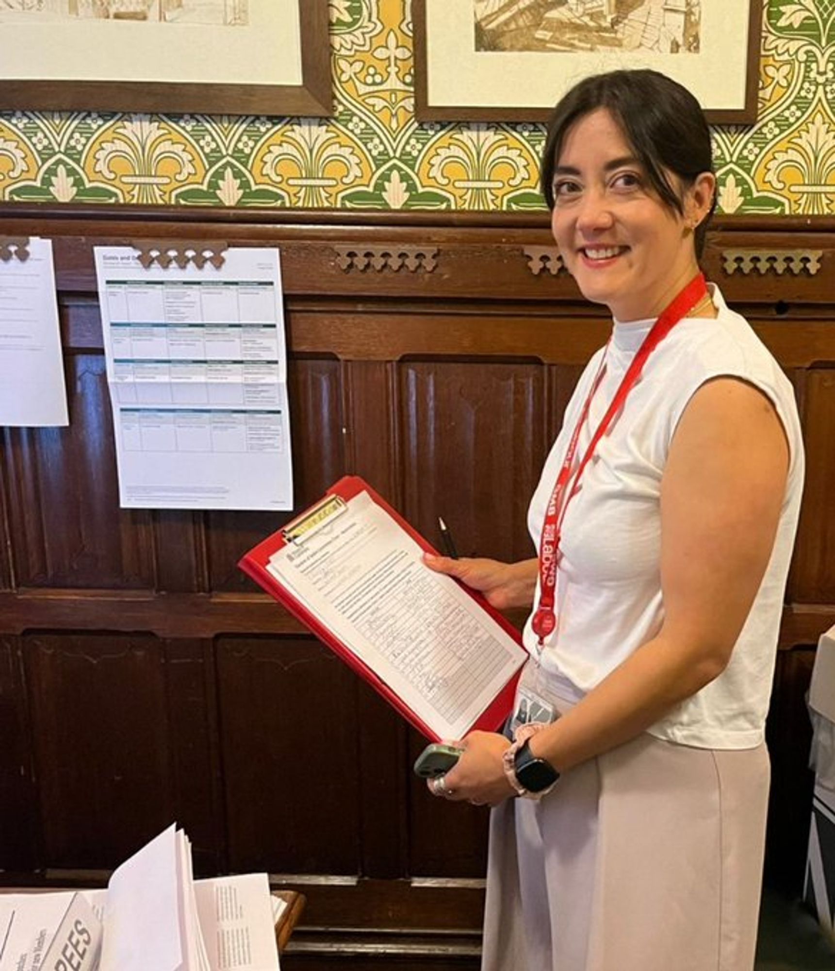 A picture of Sarah Owen MP in an oak-panelled room in the Houses of Parliament, holding her nomination papers for Chair of Women and Equalities select committee, smiling to the camera.