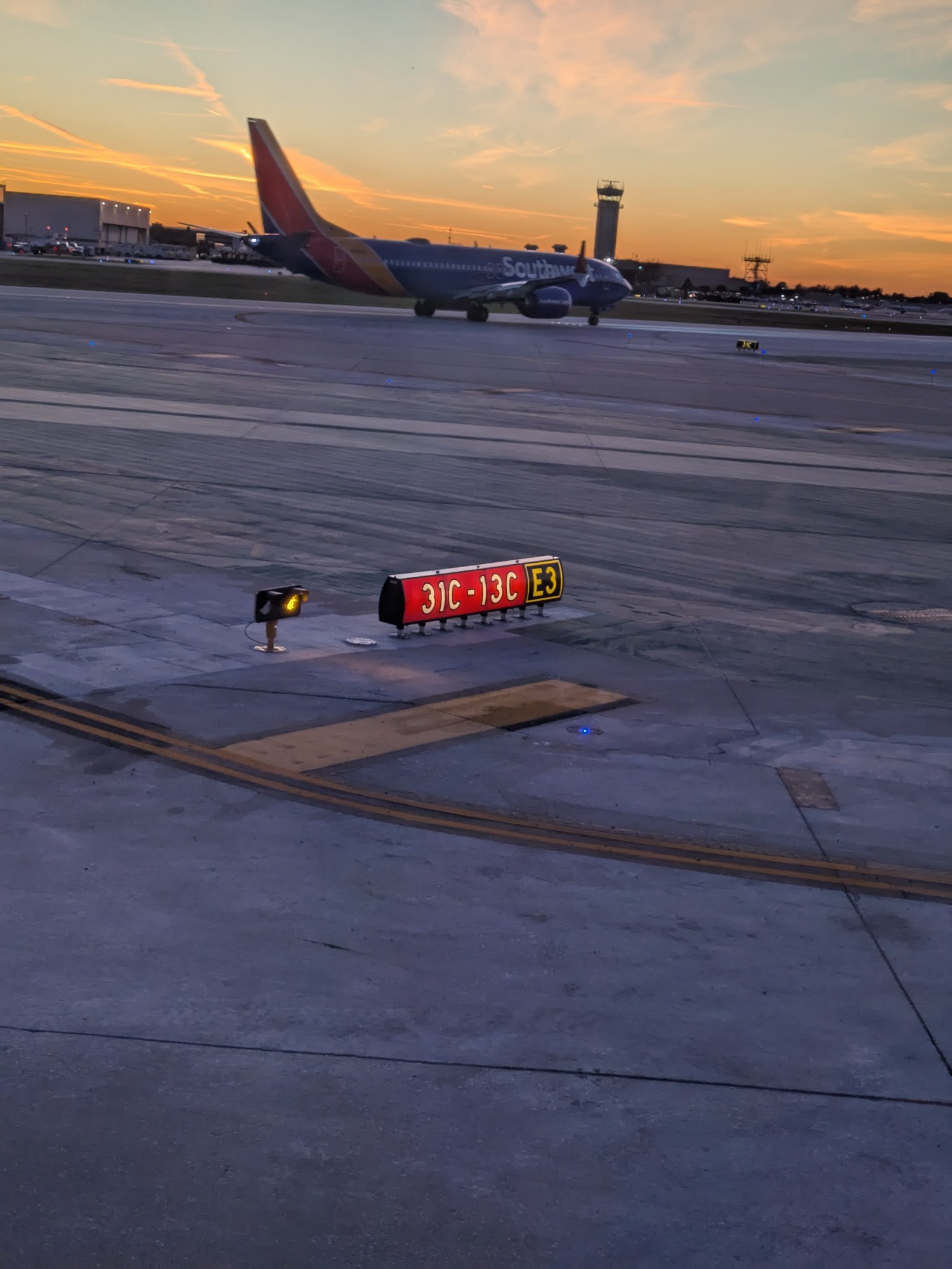 Sunset sky WI h a plane and airport control tower. A runway sign in the foreground 