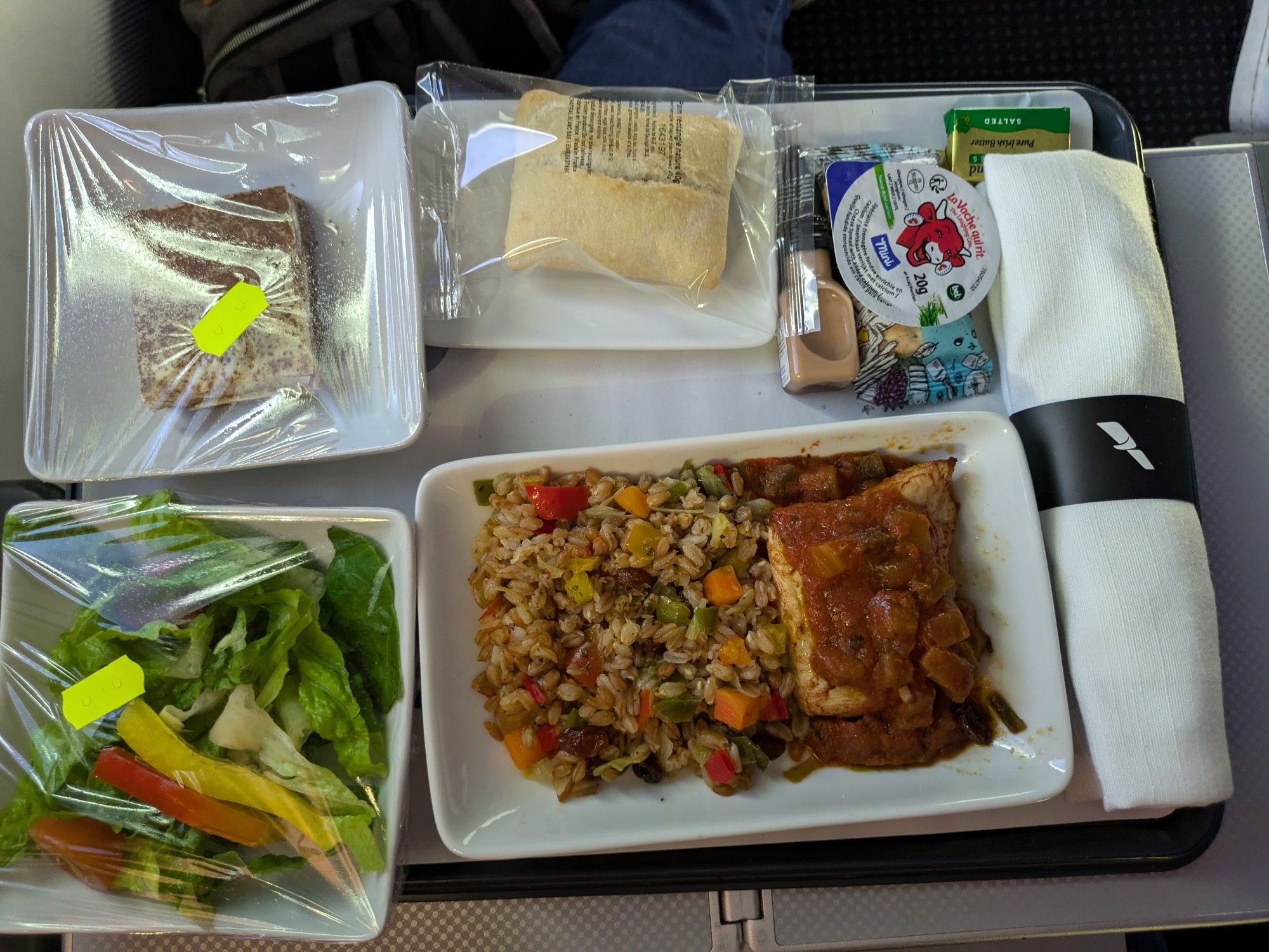 Airplane meal on a tray table with several square/rectangle plates and lots of plastic wrap