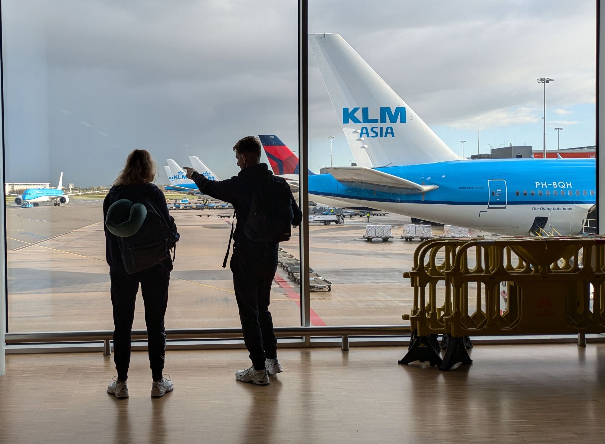 Silhouette of a couple in front of floor to ceiling windows with KLM and Delta planes outside