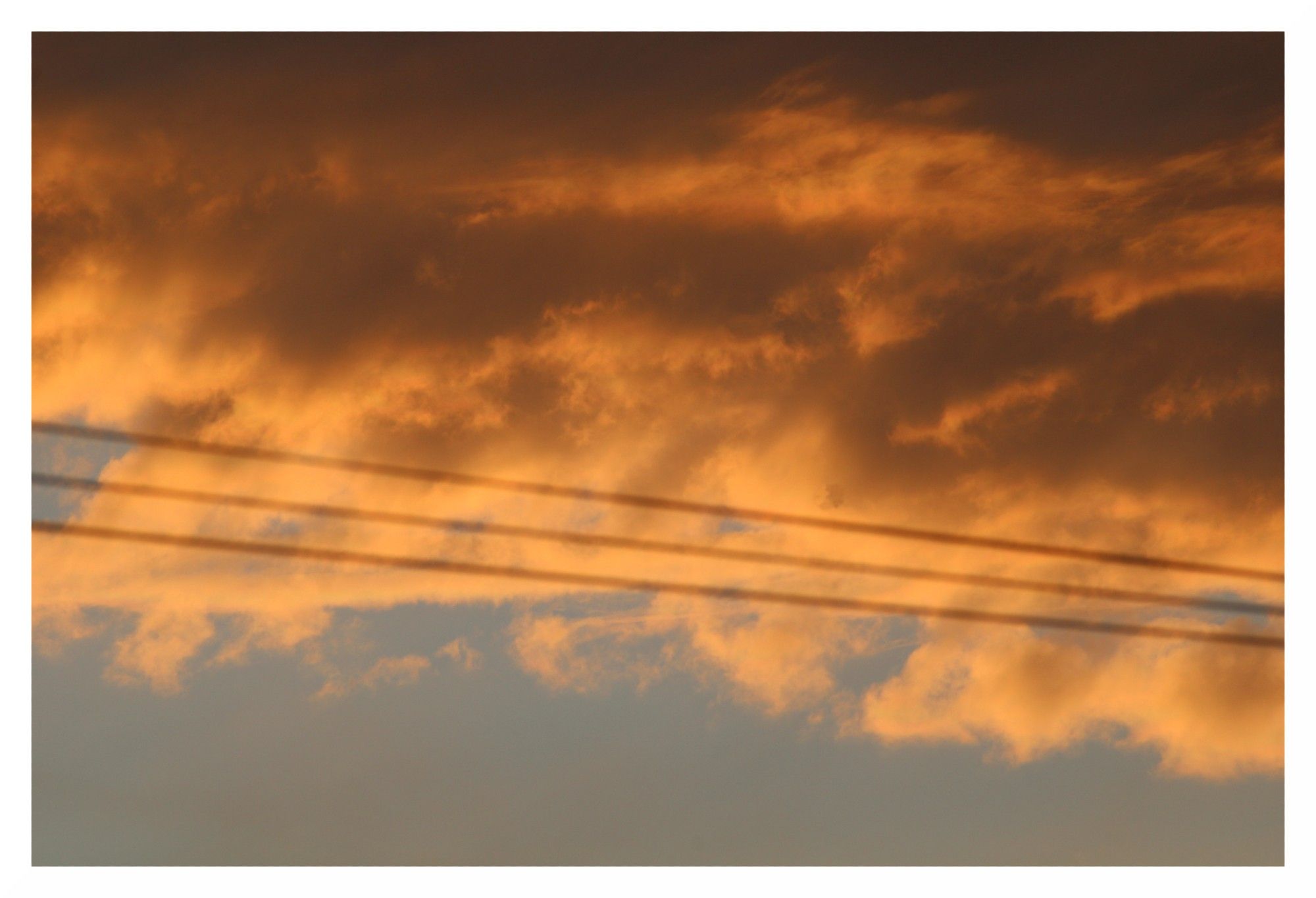 Clouds lit up orange by the sun, with three parallel wires crossing from left to right and blue sky at the bottom.