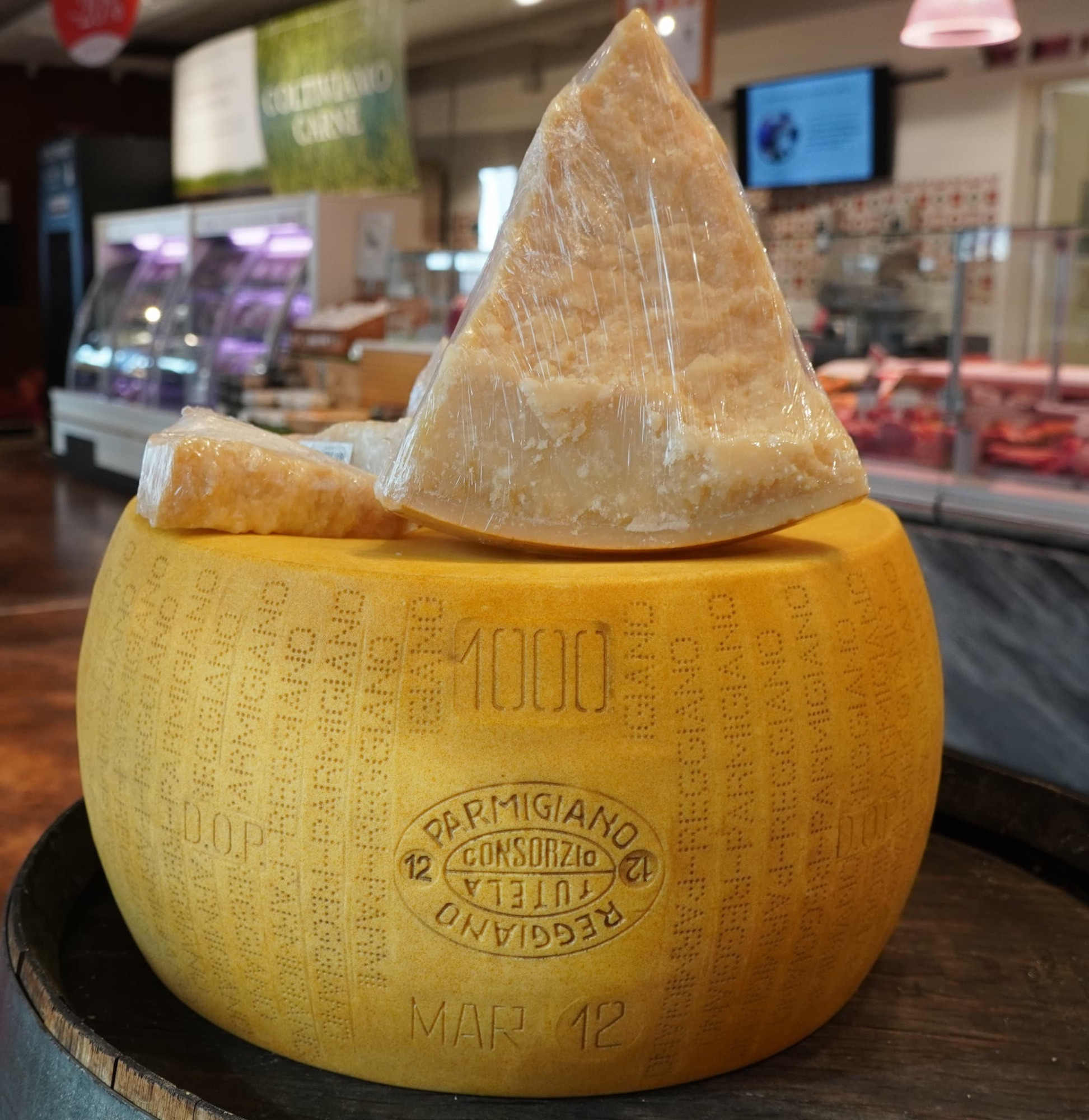 A wheel of parmesan cheese with more parmesan cheese on top in a market

Naturpuur, CC BY-SA 4.0 <https://creativecommons.org/licenses/by-sa/4.0>, via Wikimedia Commons