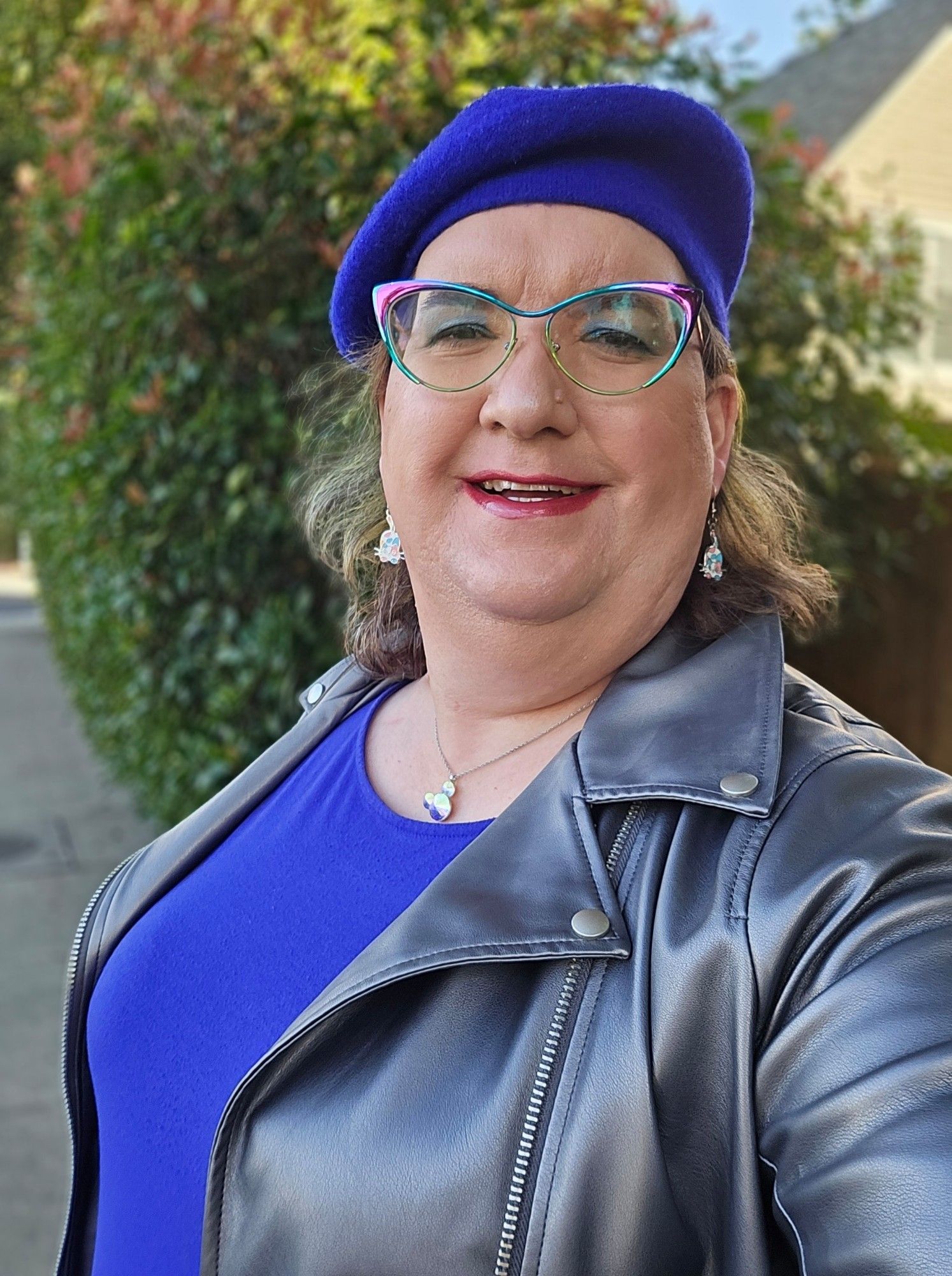 Selfie.  Royal blue beret.  Mickey Mouse head necklace.  White kitty earrings with trans colored spots.  Blue dress.  Faux leather silver jacket