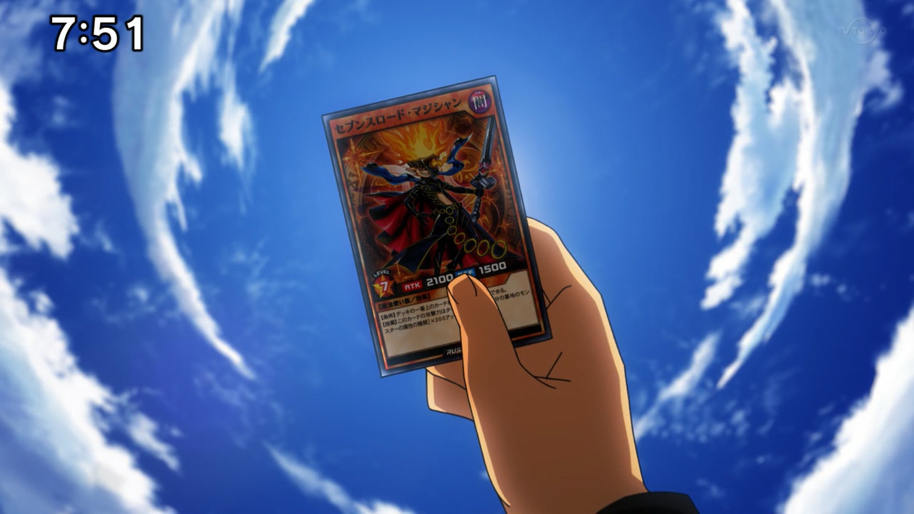 A screenshot from the Yu-Gi-Oh! SEVENS anime, taken from episode 92. No character is visible in it, but it depicts Luke holding up a monster card to the sky from his point of view, while he's lying down on the ground all alone; the card in question is Sevens Road Magician, which Yuuga left with him before leaving two years prior. The card is being held up at the very center of the screen, covering the sun behind it; all around it is the blue sky filled with clouds.
No subtitles are present in this image.