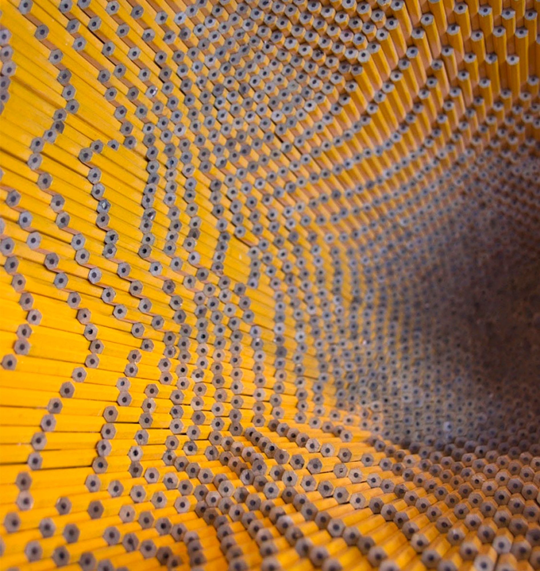 a detail of a sculptural vessel made from pencils, with the yellow paint showing inside