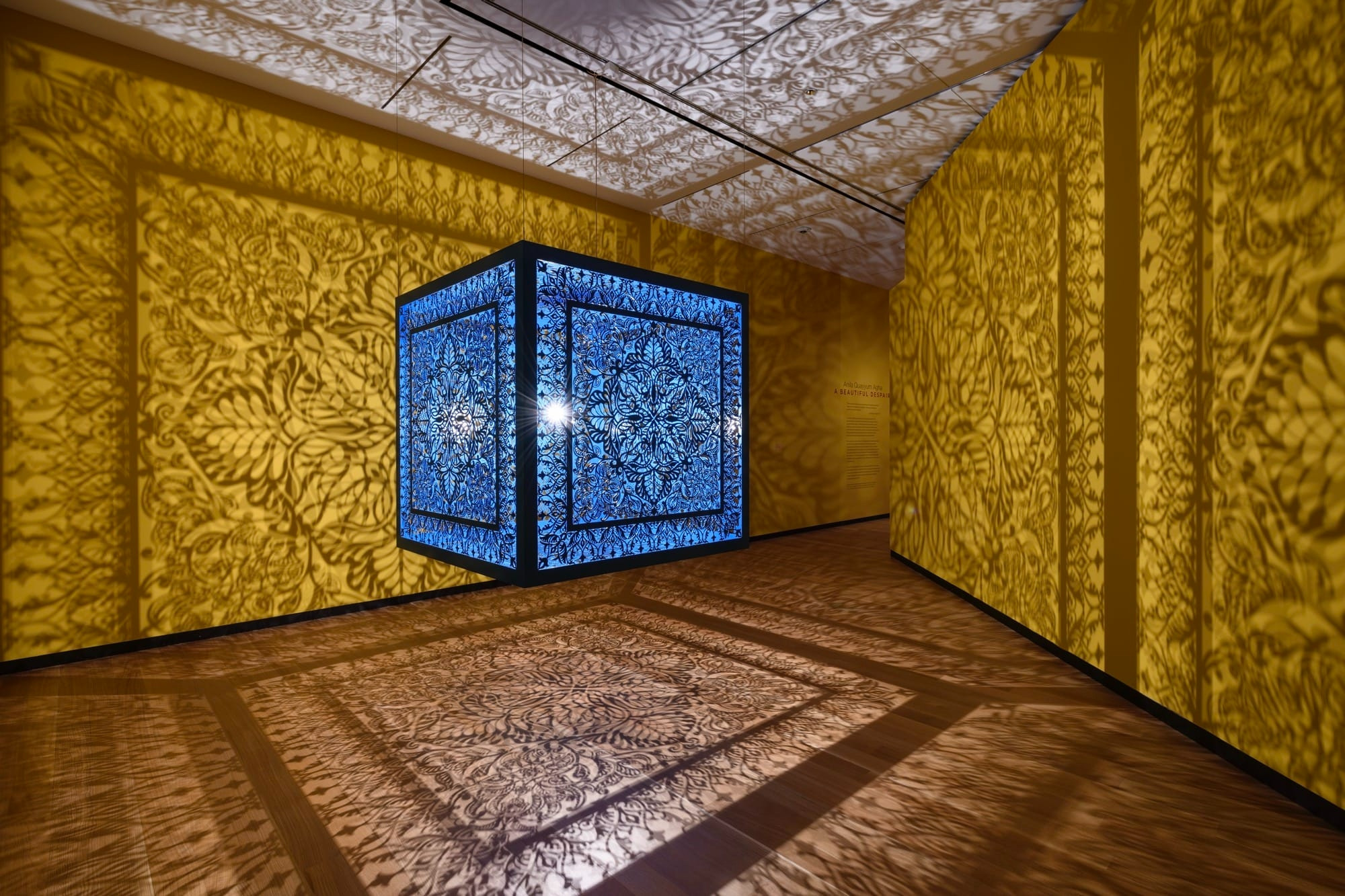 a sculptural installation in a yellow room, with light emitting from within a structure that casts ornate shadows onto the walls