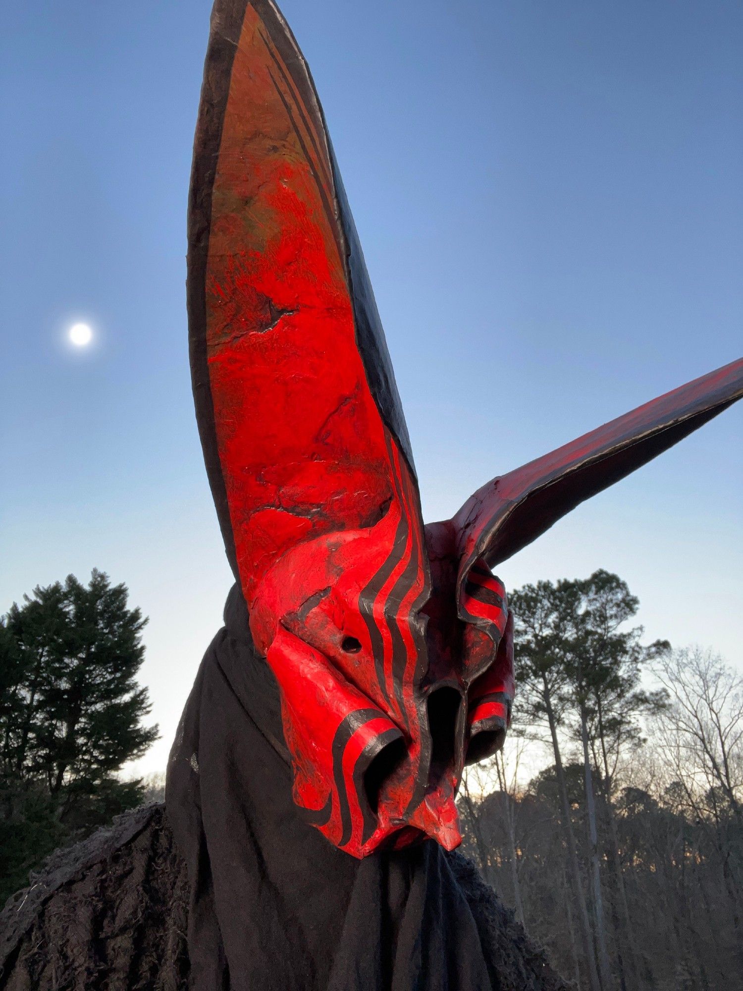 a portrait of a person wearing an ornate, red, papier mache bat mask