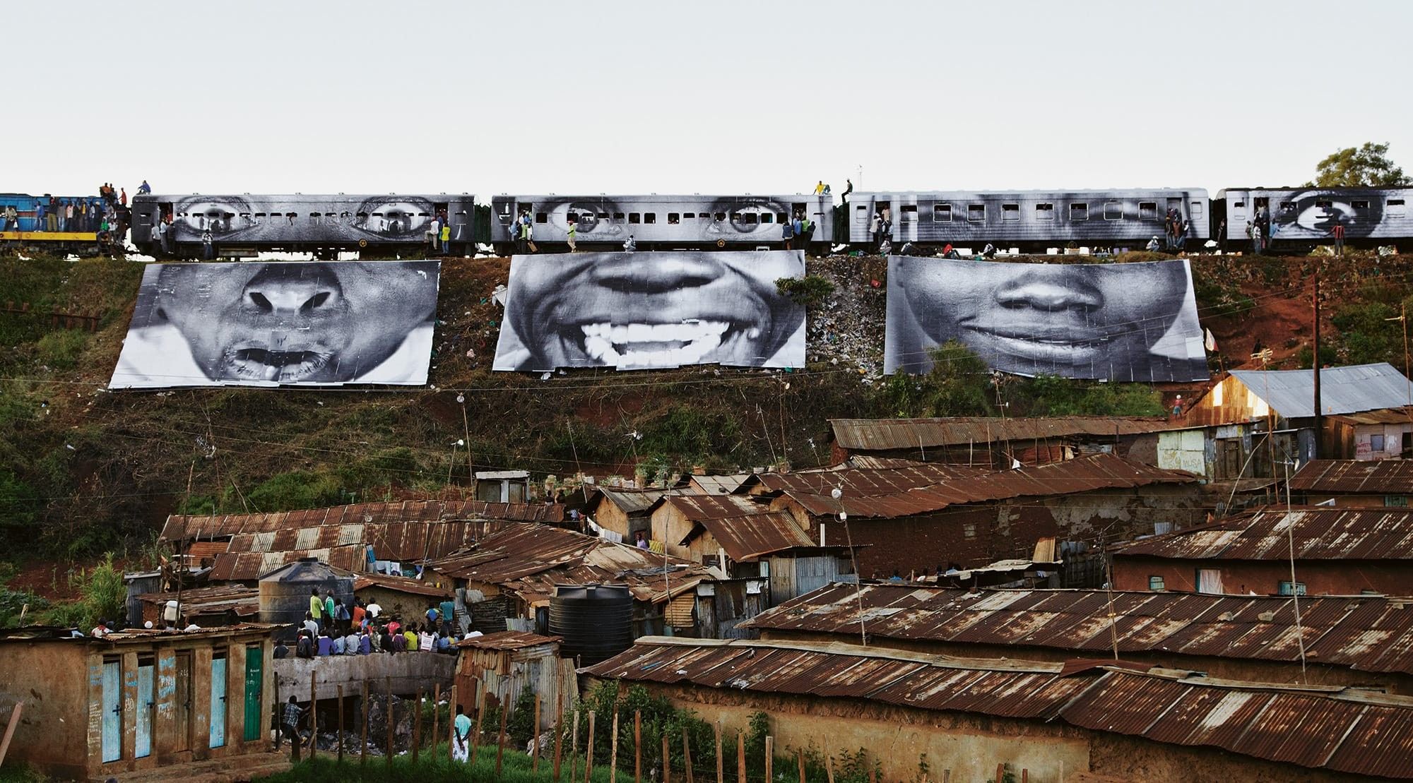 a procession of train cars above a village depicts 3 large black and white photographs of expressive faces