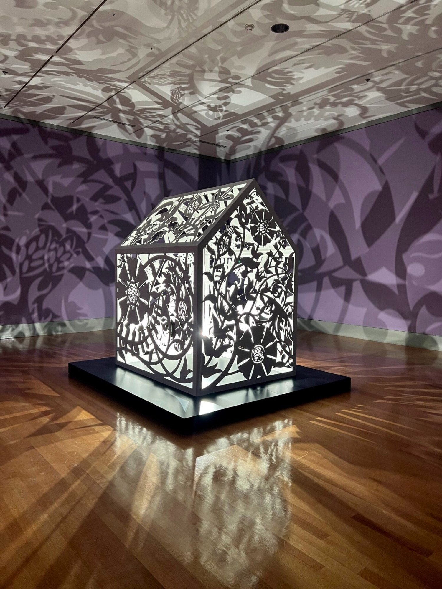 a sculptural installation in a violet room, with light emitting from within a structure that casts ornate shadows onto the walls