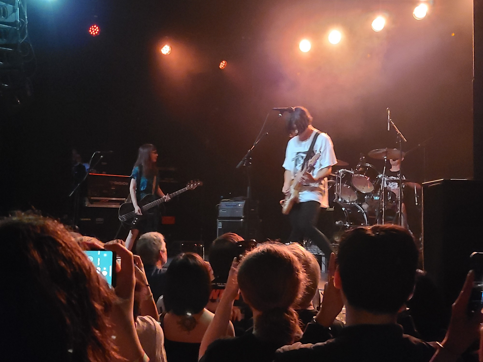 Band members of MASS OF THE FERMENTING DREGS on a dimly lit stage. Photo from the audience, front left of the stage.