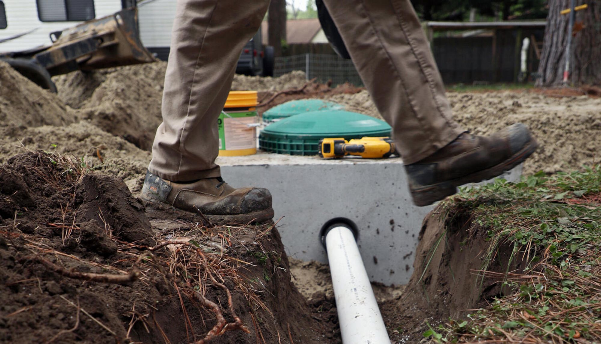 Ground level image of septic system installation with person in work boots and pants stepping over pipe