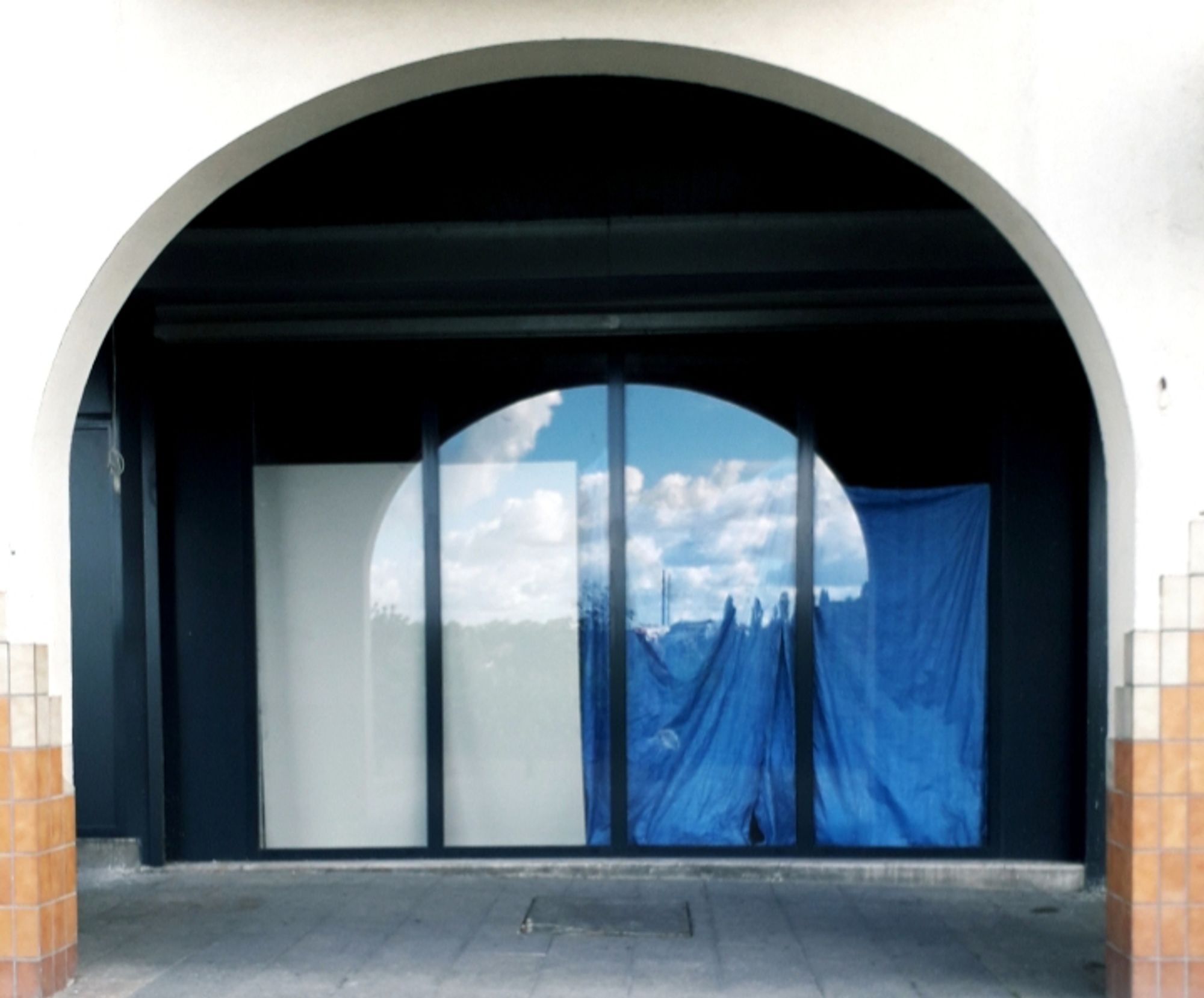 Sous une arcade, une vitrine dans laquelle se reflètent des nuages