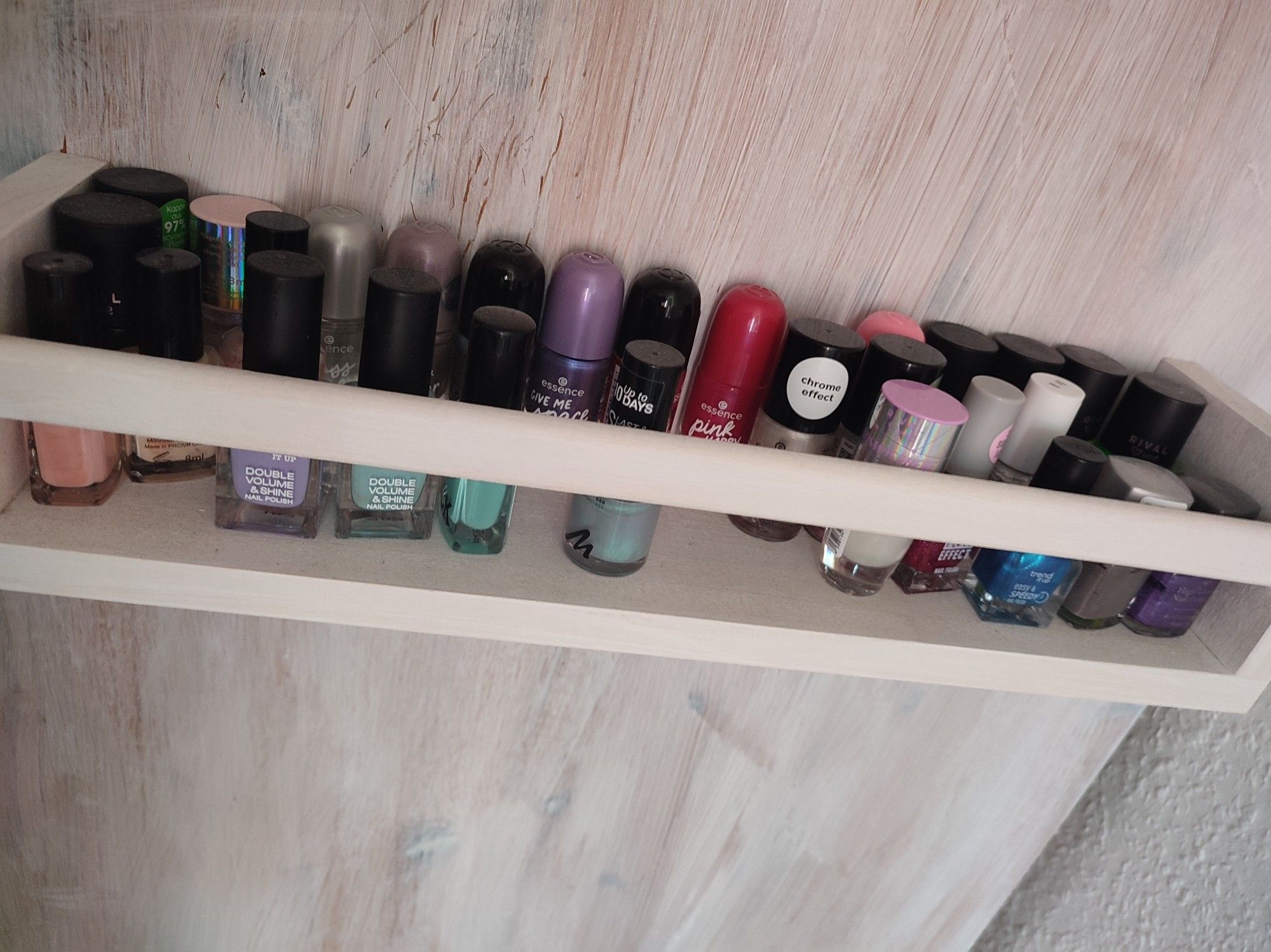 Little white shelf with nail polish bottles, currently sorted by shape/brand, rather than color. They are standing in two rows, it looks a little messy.