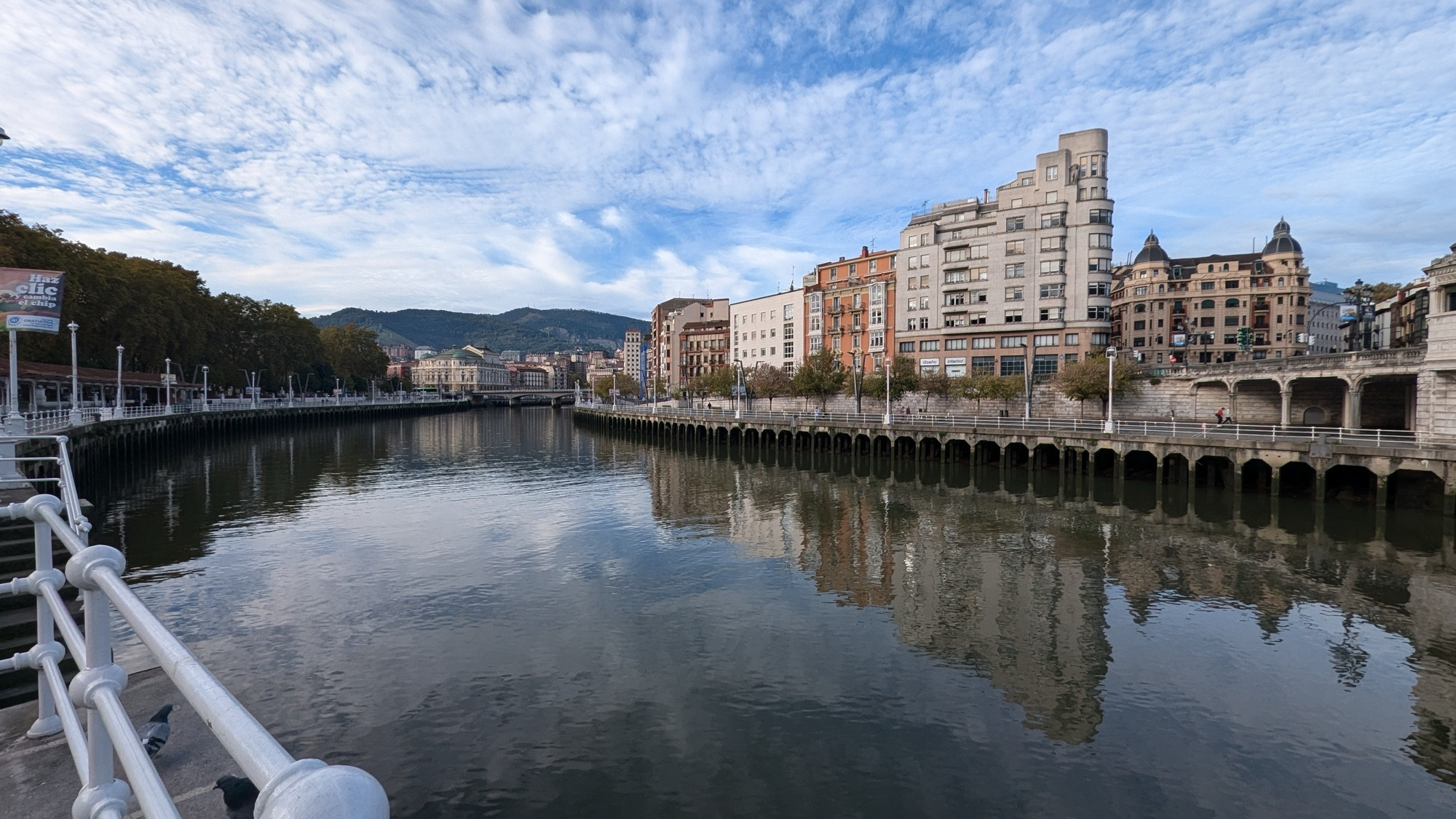 Foto a 0,5x de la Ría de Bilbao con el agua reflejando el cielo cubierto de nubes  poco espesas 