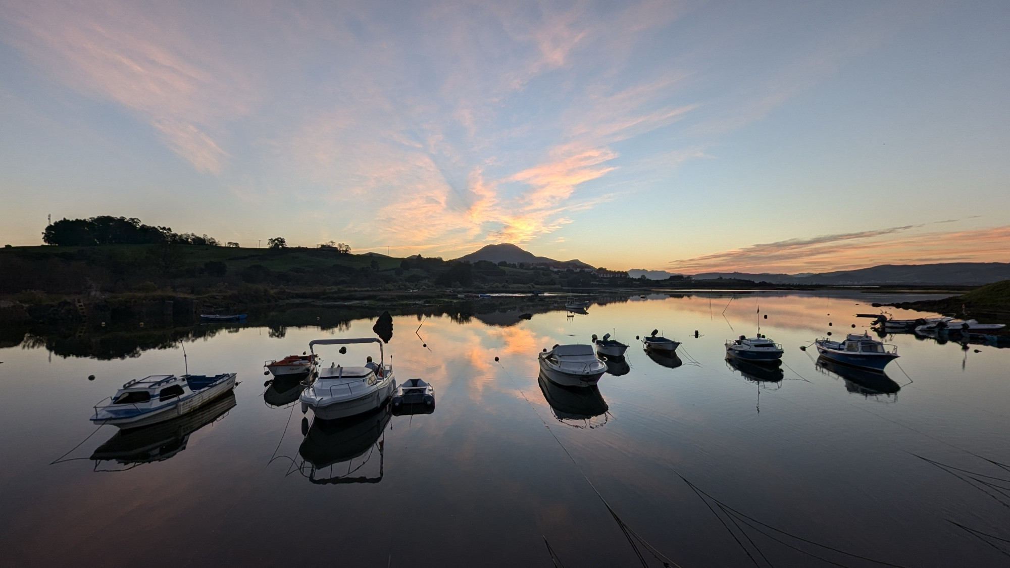 Foto a 0,5x del embarcadero de Ancillo al amanecer con el agua reflejando el cielo con nubes iluminadas por el Sol