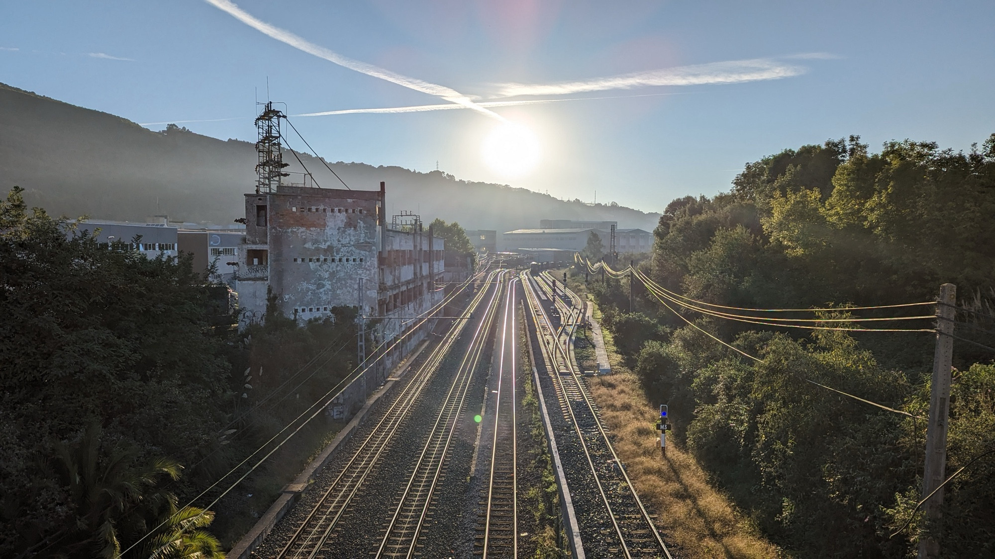 Foto del paso de vías de tren de Euskotren en Basauri con Sol brillando en el cielo