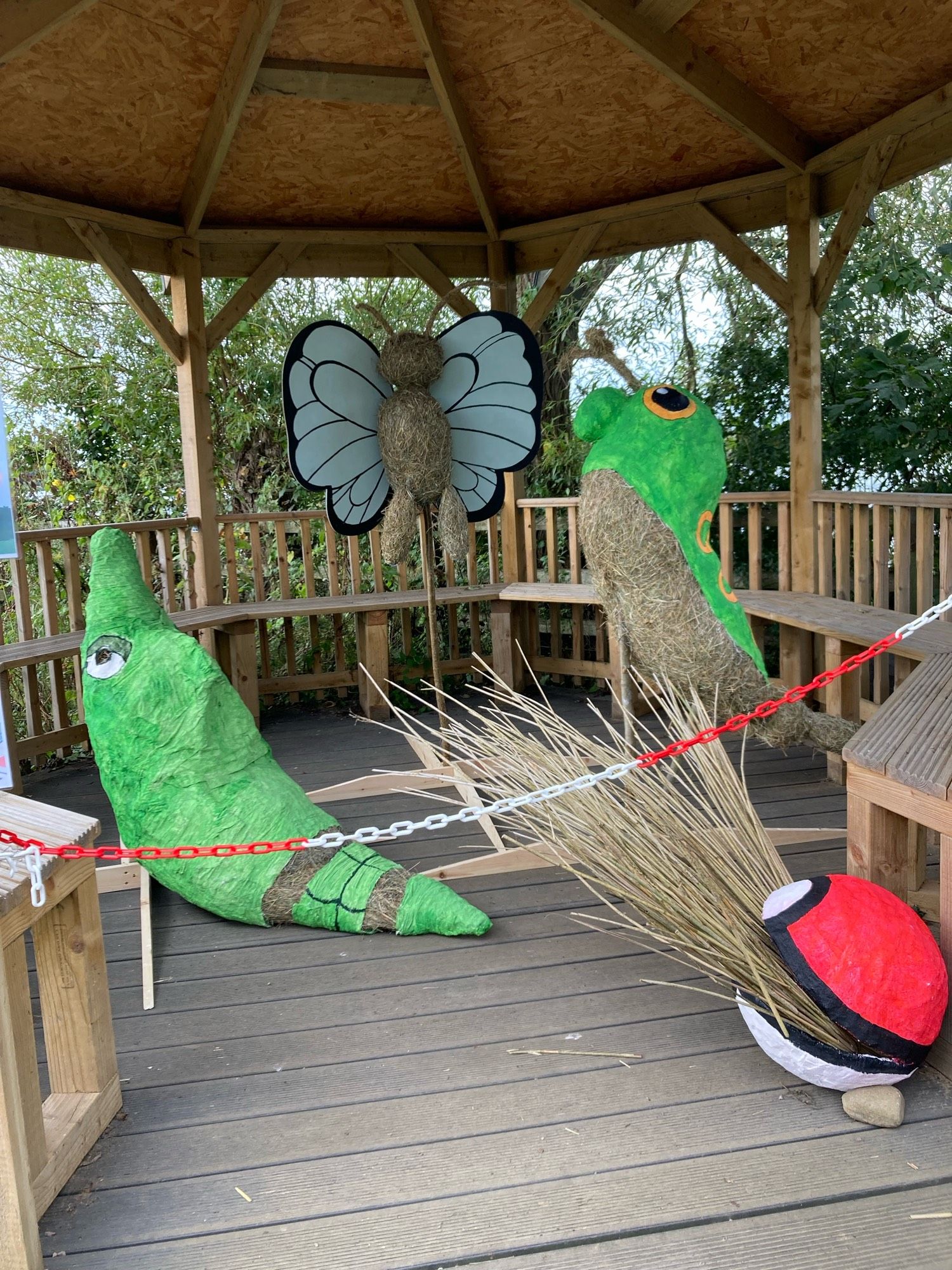 Scarecrows of Metapod, Butterfree, Caterpie, and a Pokeball in a wooden gazebo.