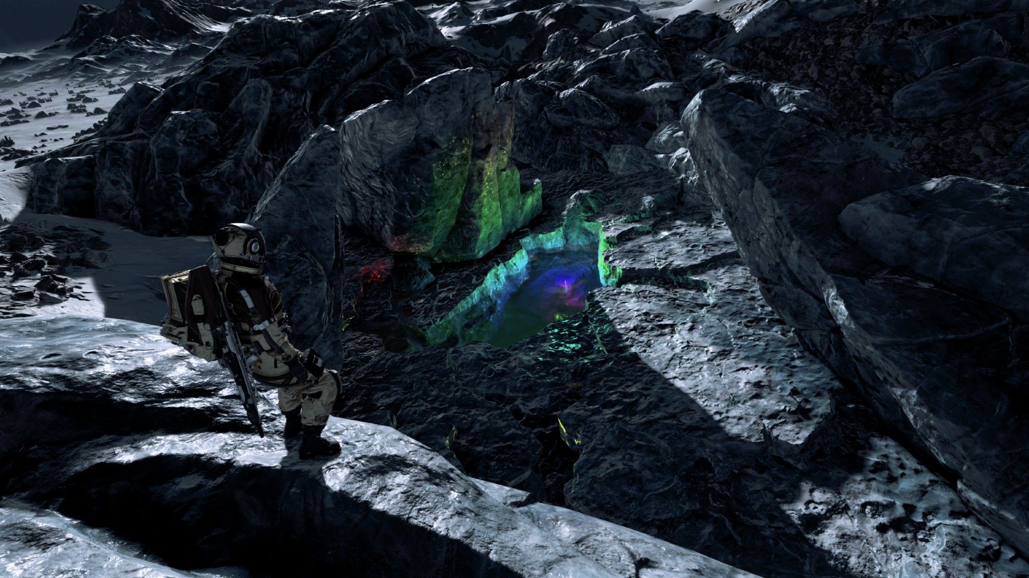 A screenshot from the game Starfield. The surface of a rocky ice planet. There is a person in a golden space suit to the left, standing above at a ledge of a pool of liquid. The liquid is glowing green, blue and purple.