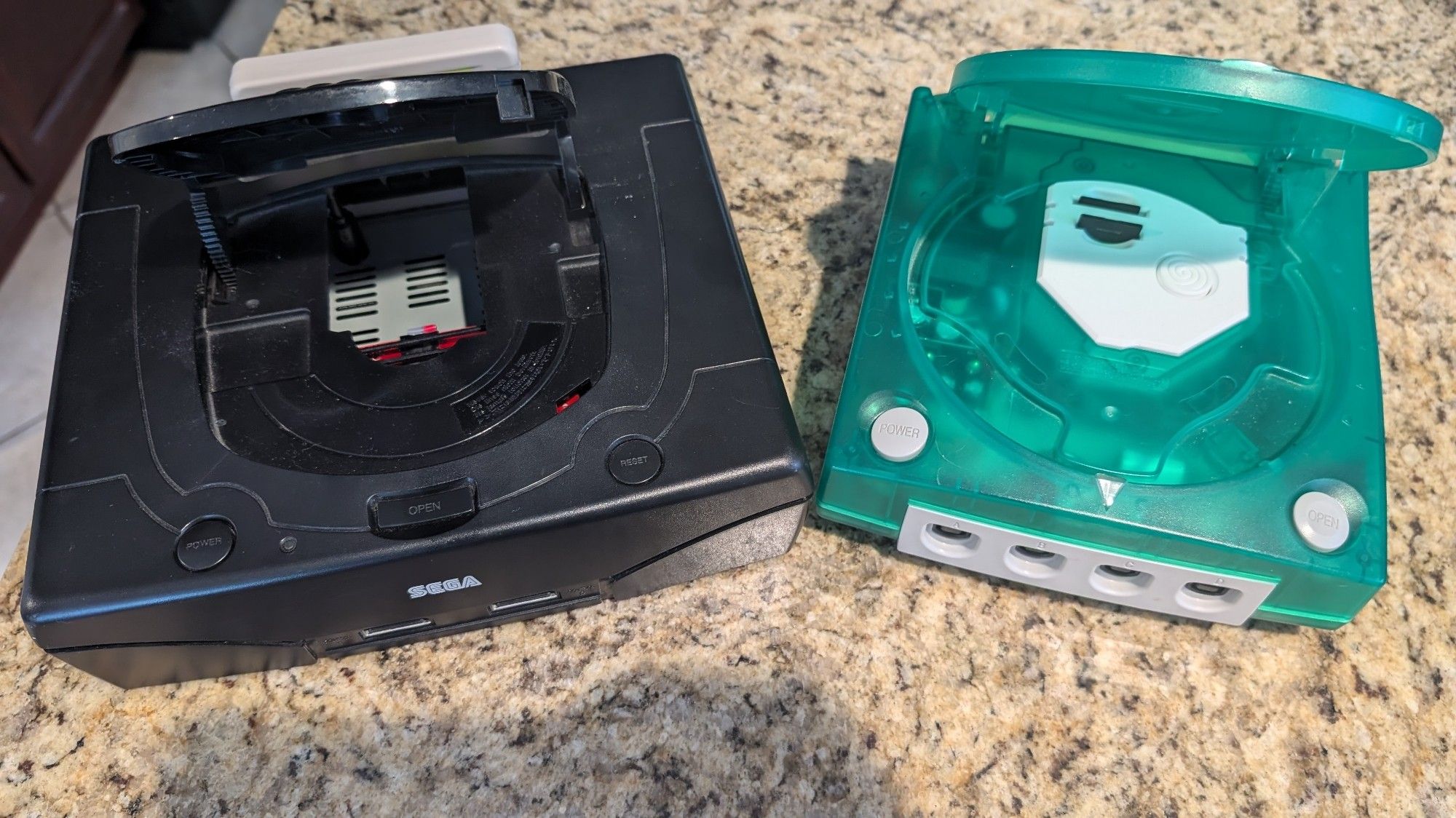 Left: Black US Model 2 Sega Saturn with a Fenrir Duo installed, Right: Green modded Dreamcast with GDEMU installed