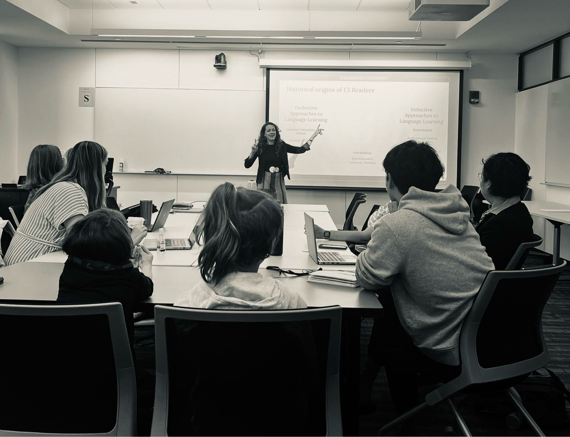 Black and white photo of me presenting in front of my dissertation committee and a few guests including my two young sons