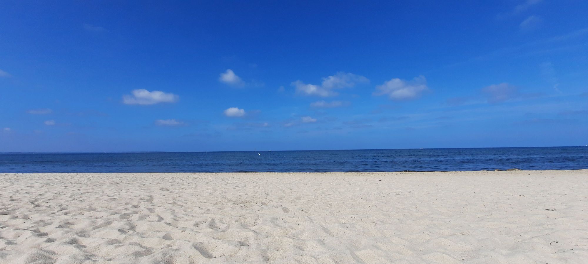 Ein menschenleerer Sandstrand. Am Himmel über dem Meer ein paar kleine weiße Wölkchen.