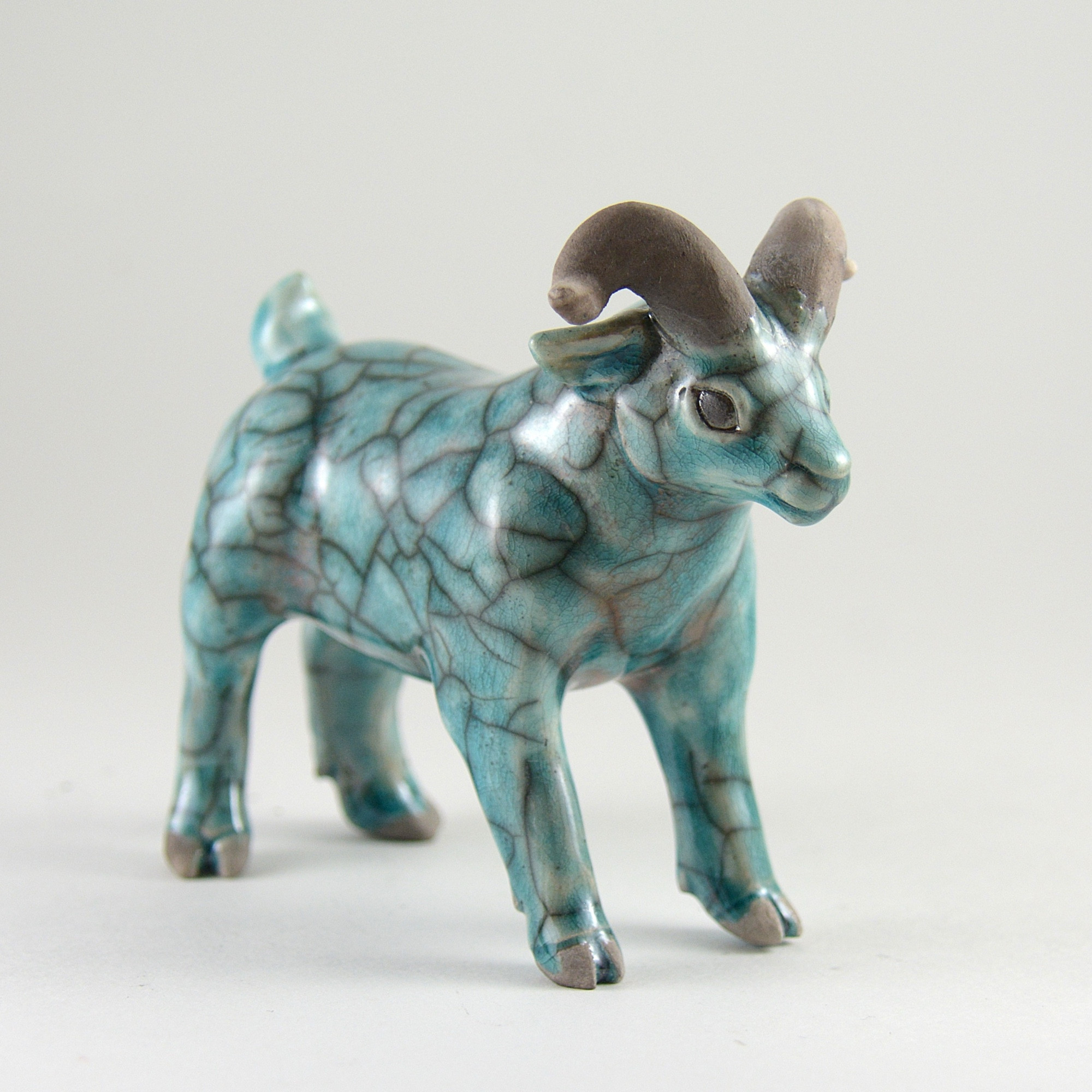 A ceramic goat sculpture on a white background. The goat has a pale blue crackled glaze.