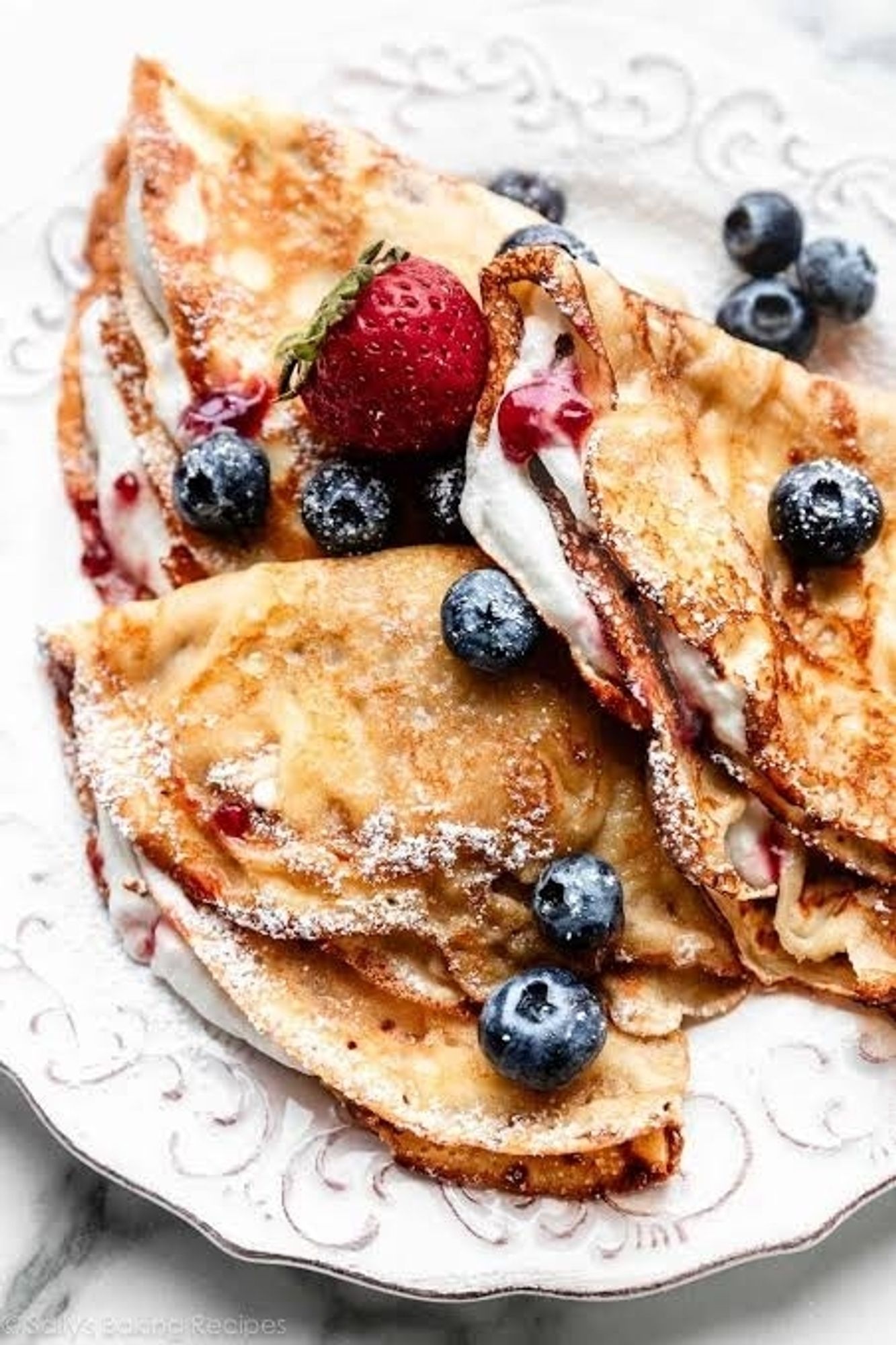 an image depicting three homemade crepes on a plate with blueberries and strawberries