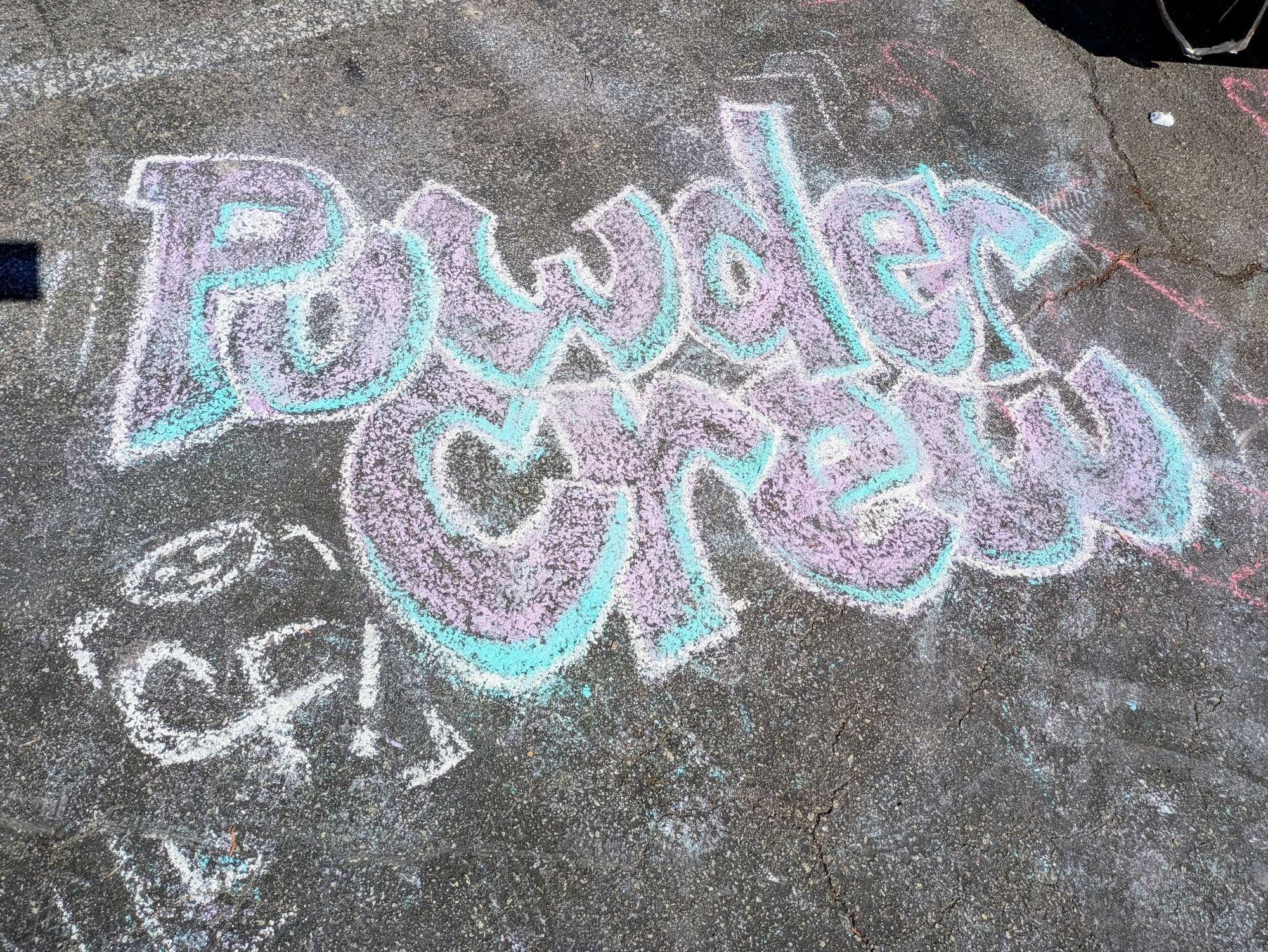 "Powder Crew" written in chalk on asphalt. It is written in a embossed graffiti style.