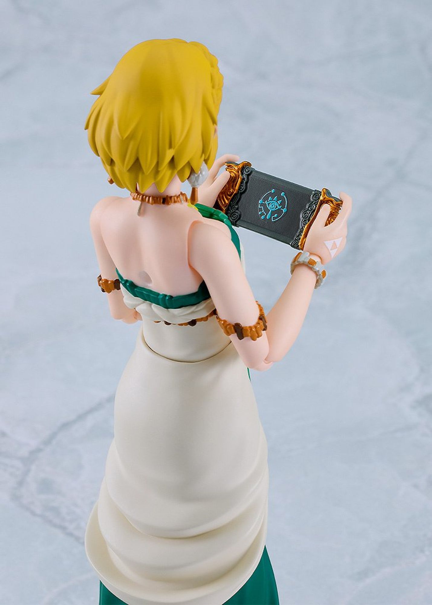 A photo of the Figma Tears of the Kingdom Princess Zelda figure. Shot from the back, Zelda holds up her Purah Pad, which looks an awful lot like a Sheikah-fied Nintendo Switch.