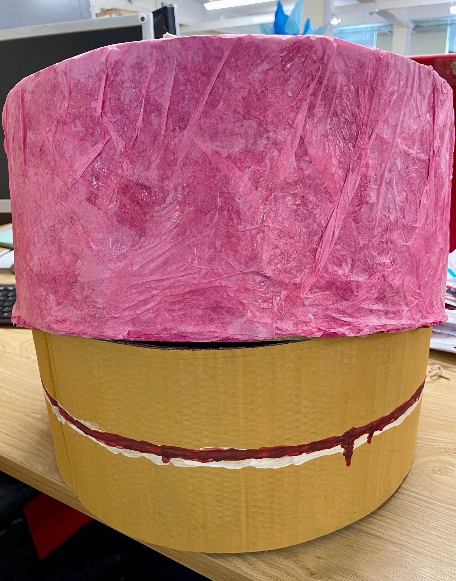 A trompe l’oeil Birthday Cake box. The bottom, inner, portion is crudely painted to look like a Victoria sponge, dribbled bits of jam included. The top part (which slides down over the bottom/inner) is covered in lots of layers pink, wrinkled and PVA glued tissue paper.