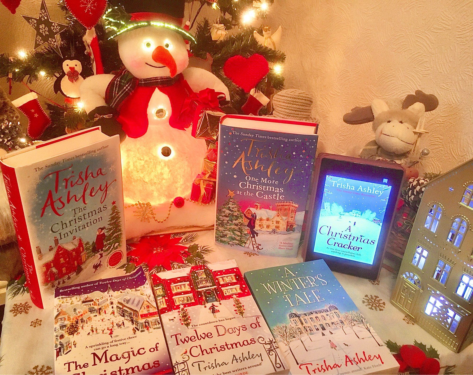 photo of a selection of fab Christmas books written by Trisha Ashley next to light up snowman and Christmas tree