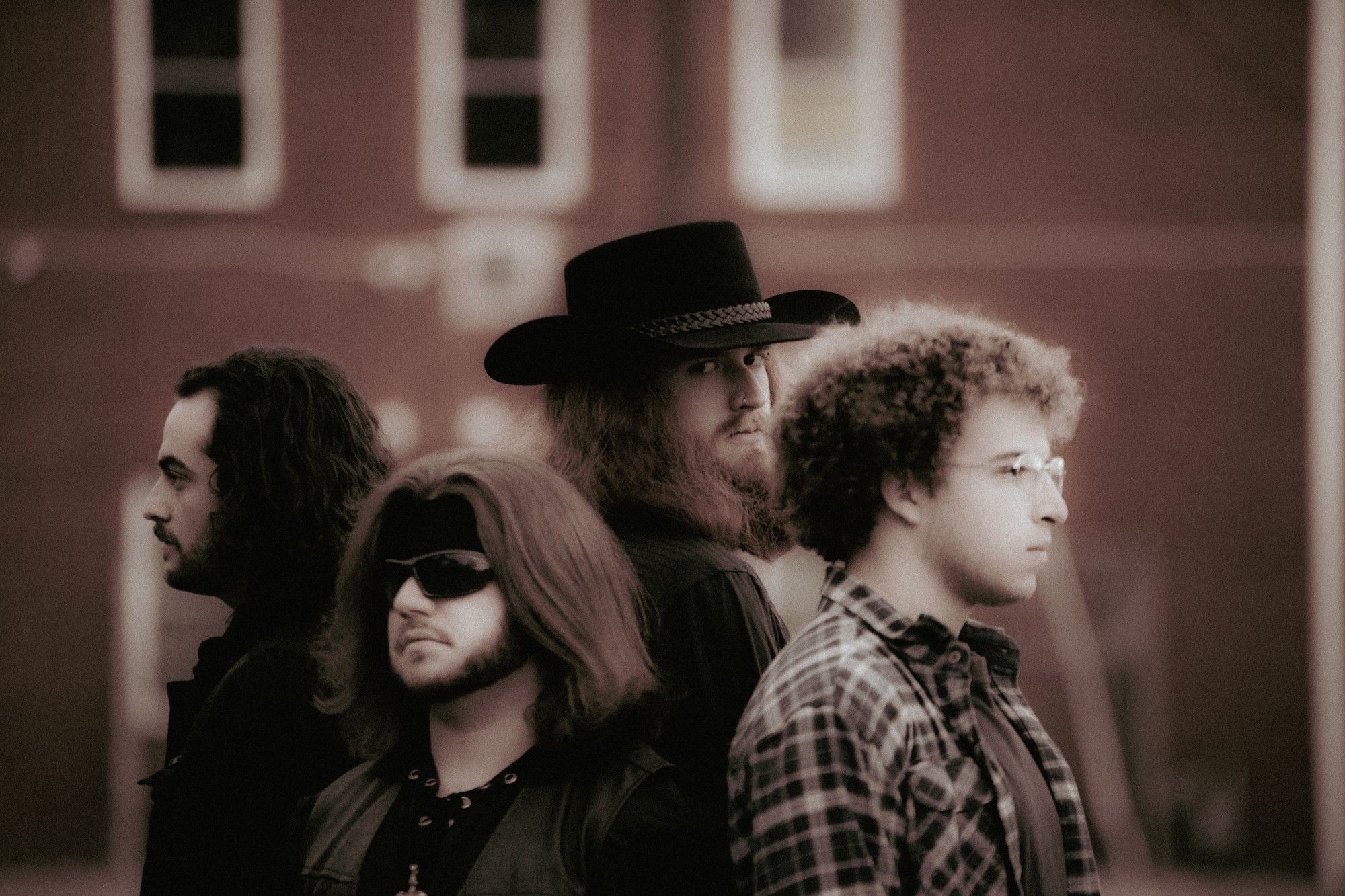 Group shot of the band, all looking in different directions. Johnny Sam Hall looks at the camera, wearing a black cowboy hat.