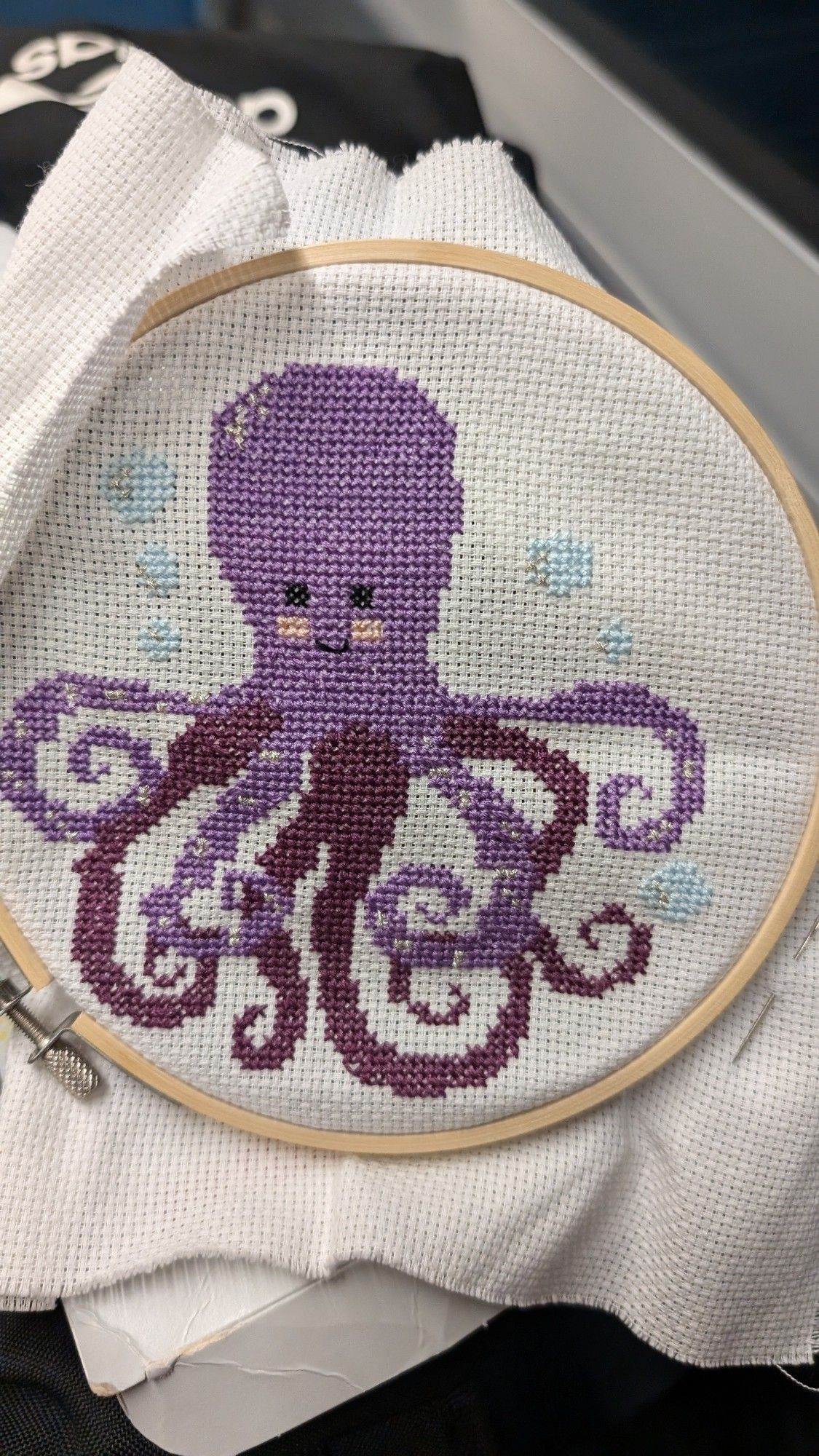 Cross stitch of a purple octopus with light blue bubbles around the edges