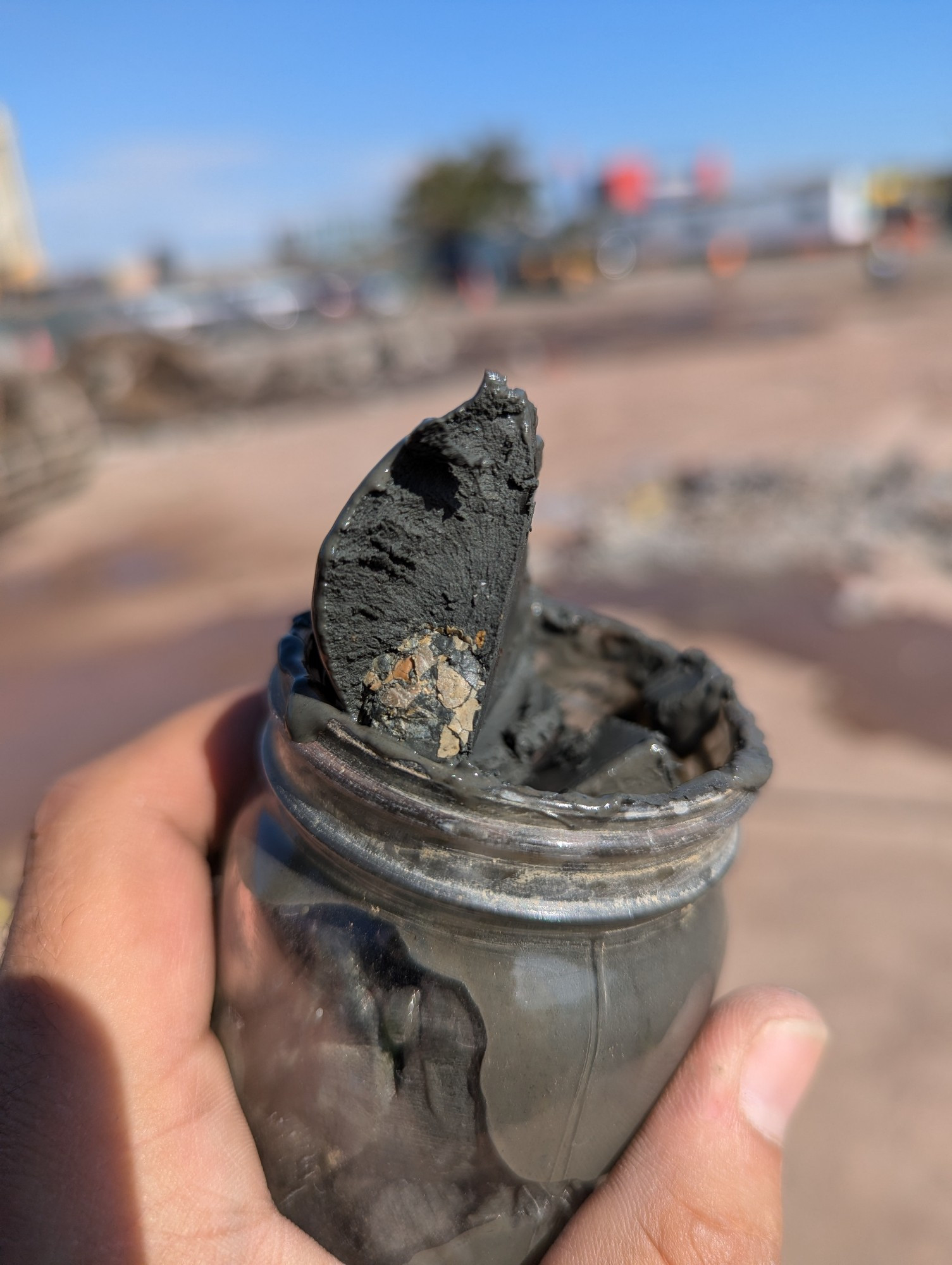 A glass sample jar with gray clay that broke on a plane perfectly and remained intact to show a circular mass of broken shells and organics matter