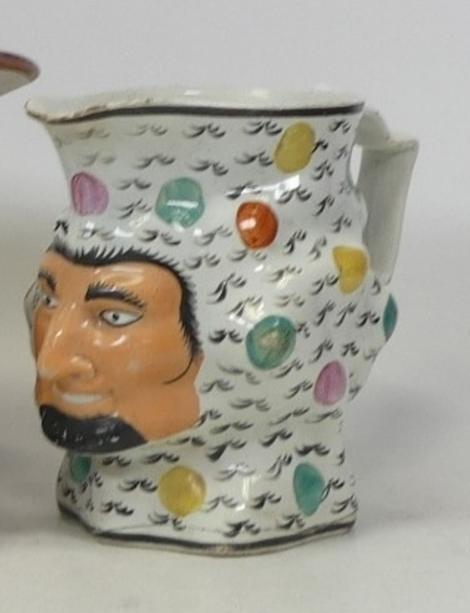 Bizarre ceramic jug in the shape of a bearded man's head covered with a strange  white and polka dot balaclava thing