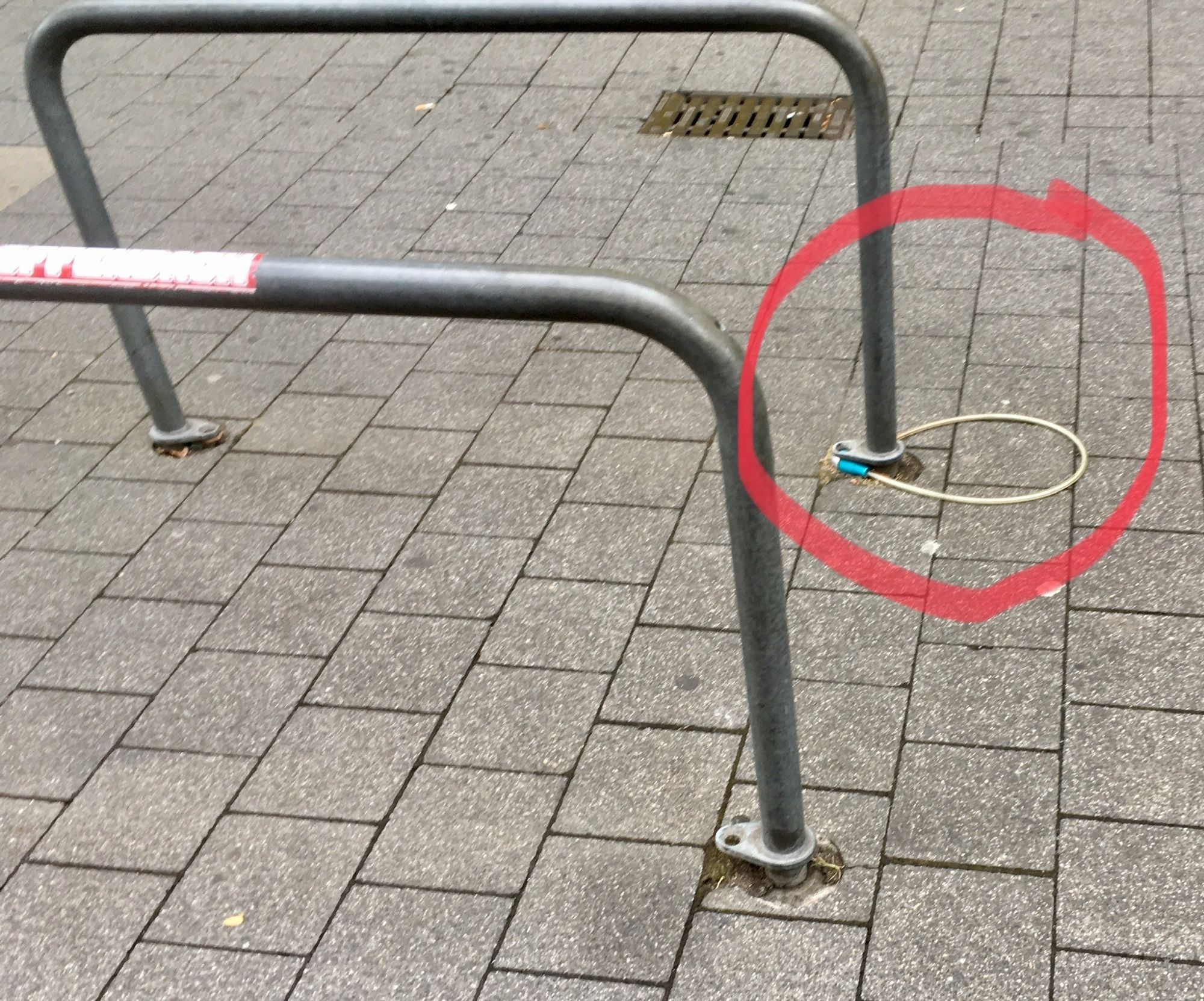 Zwei Fahrradbügel in einer Fußgängerzone. Die Bügel sind nicht im Boden verschraubt. Ein Bügel hat ein "Schloß" am Boden liegen (rot eingekreist).