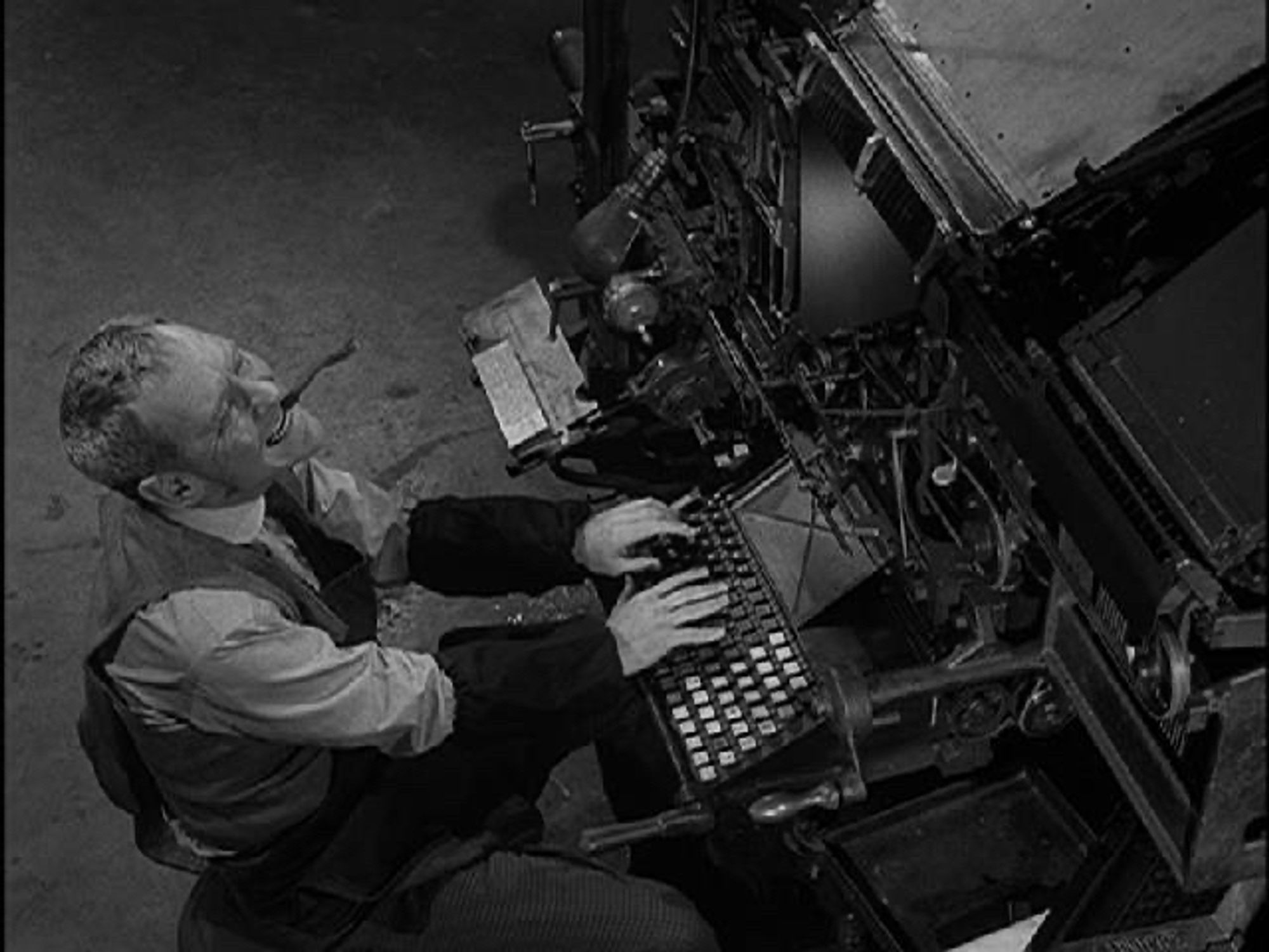 Burgess Meredith at a typesetting machine, smiling, with a cigar in his mouth, in the Twilight Zone episode 'printer's devil'