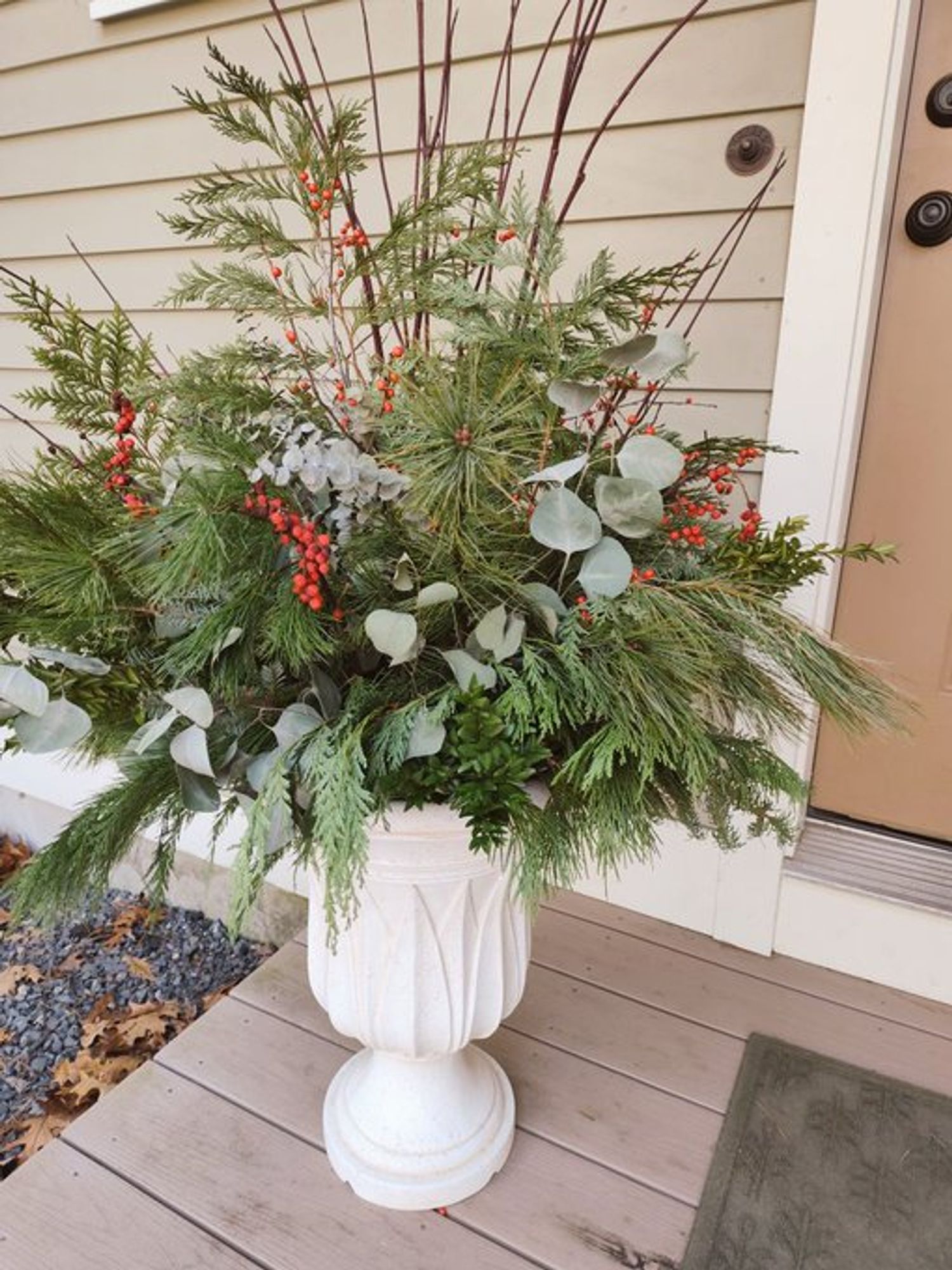 An ivory urn with a tall arrangement of evergreen branches, eucalyptus, and red ilex berries.